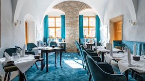 Ein Restaurant mit einem steinernen Bogen, blauen Samtstühlen und gedeckten Tischen.