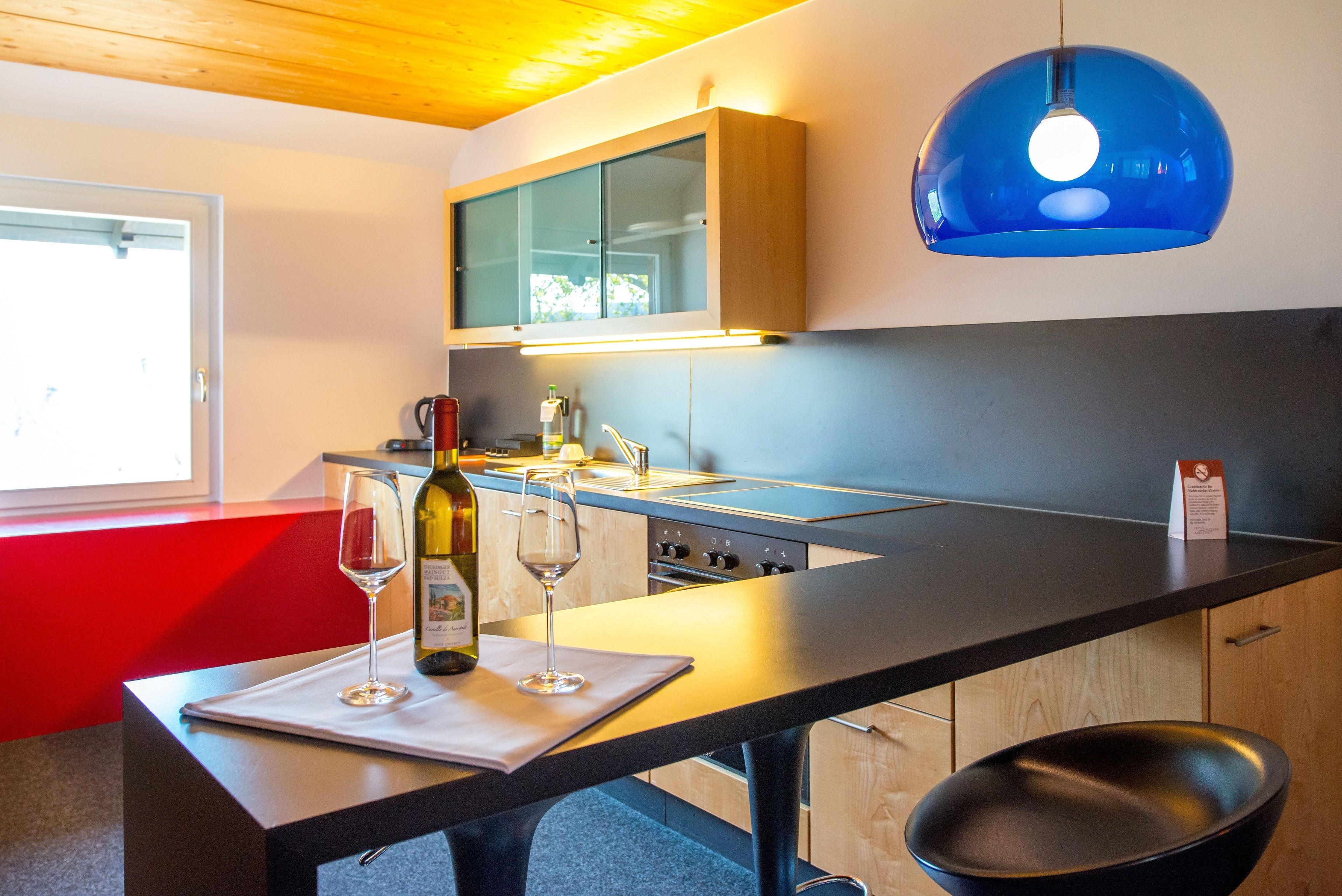 A modern kitchen with a black countertop, a wine bottle, and glasses on a mat.