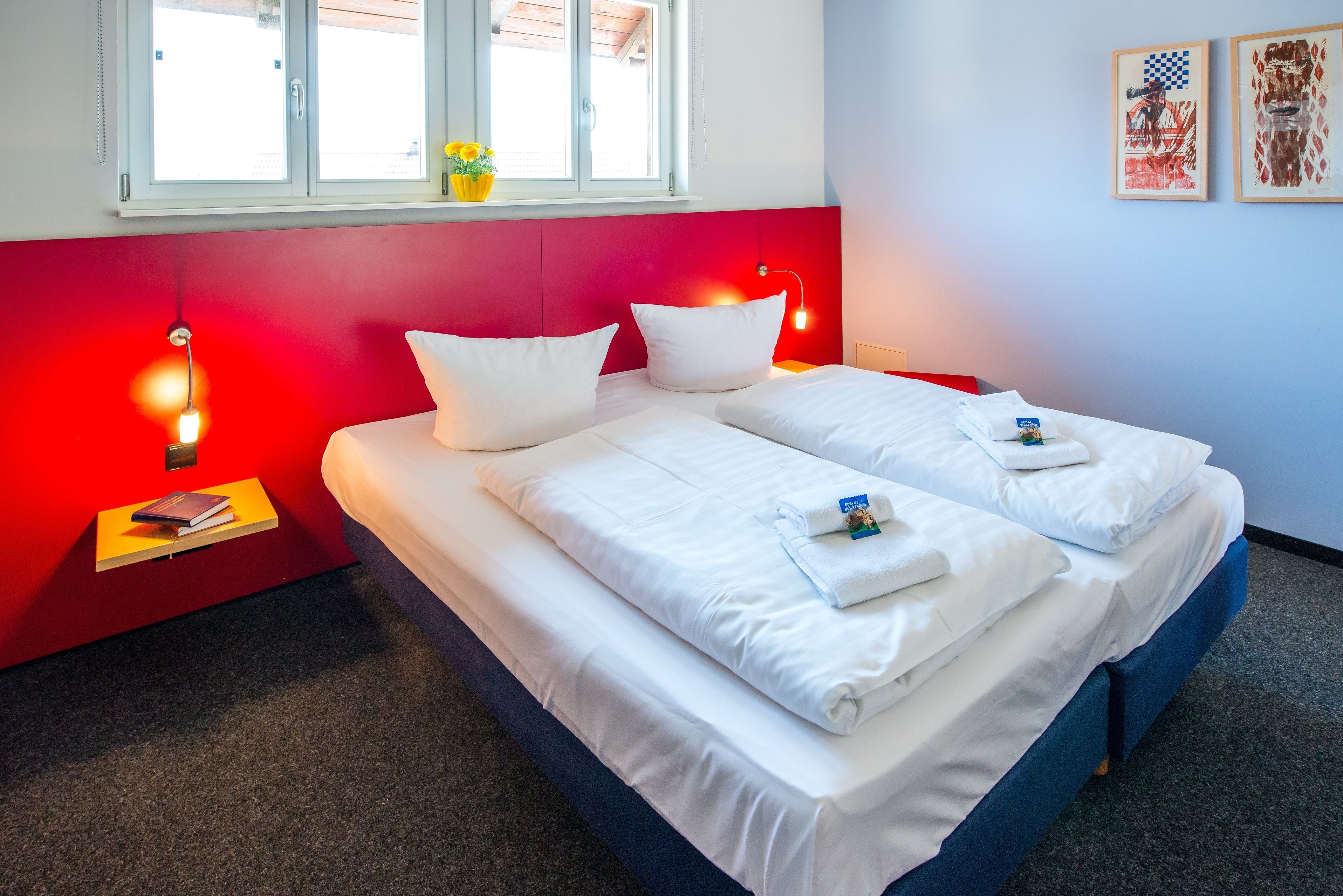Un lit double avec du linge de lit blanc, un mur d’accent rouge et une fenêtre donnant sur un beau paysage.