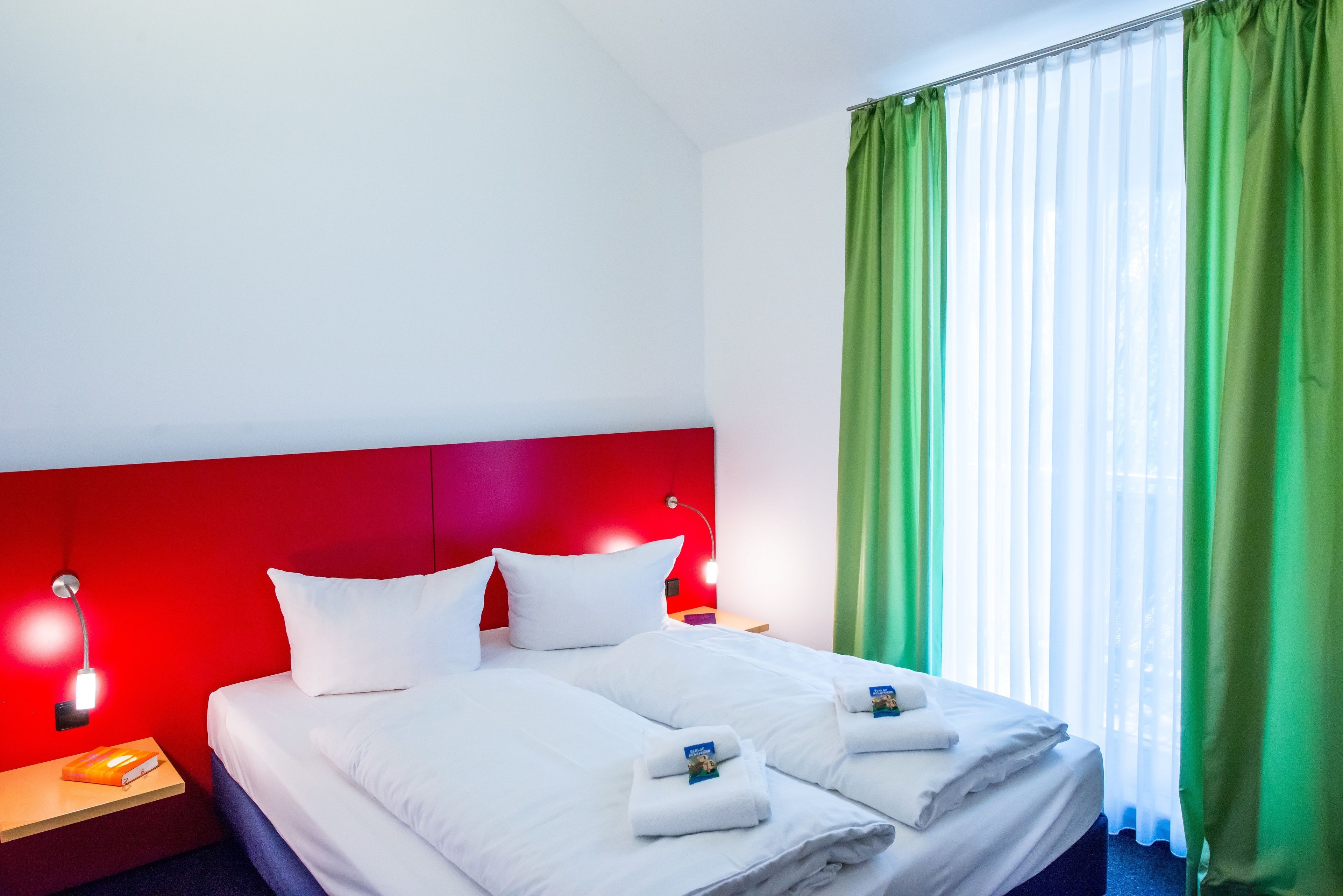 Una habitación de hotel con cabecera roja, ropa de cama blanca y cortinas verdes.