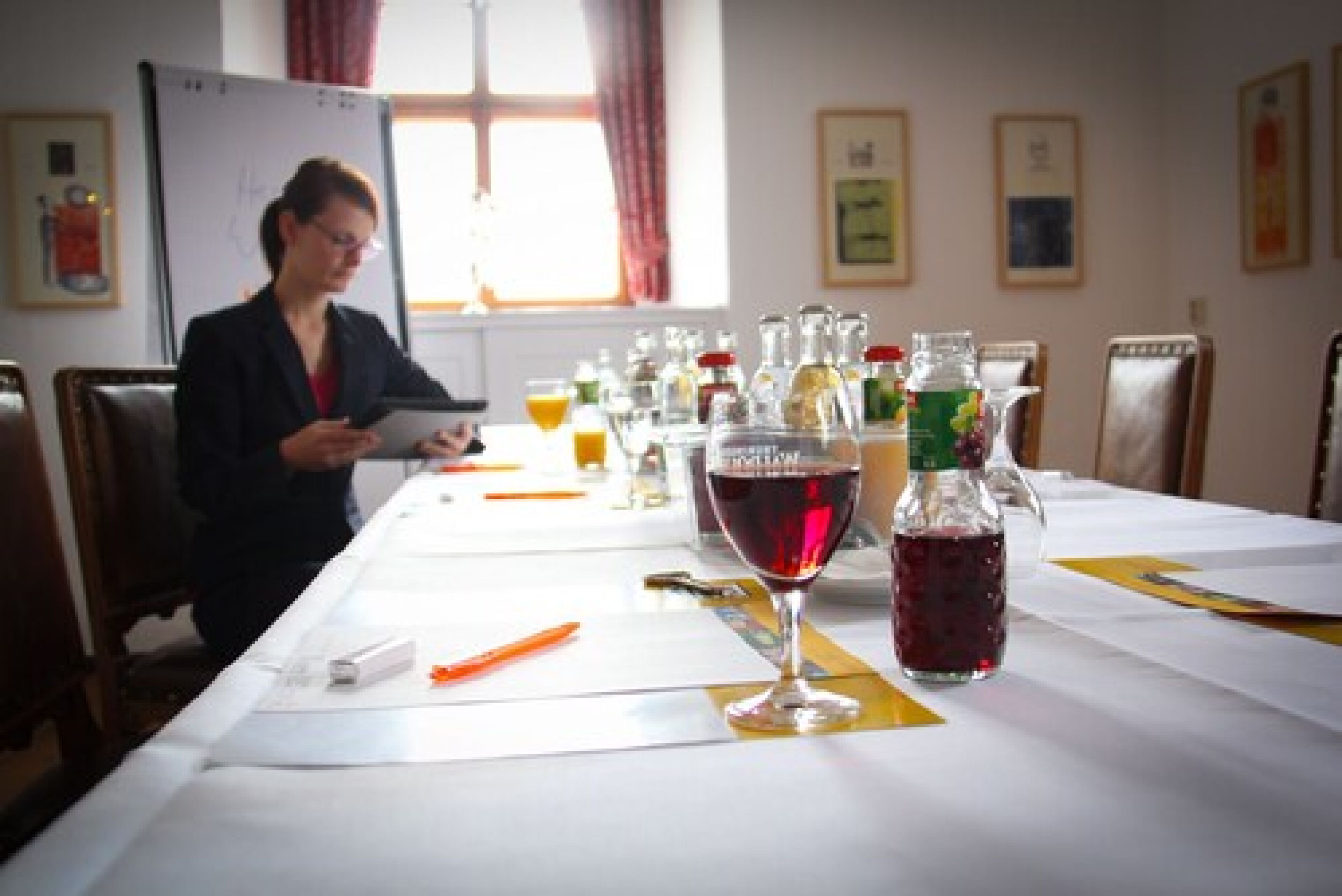 Ein Konferenzraum mit einem langen Tisch, verschiedenen Getränken und einer Person, die ein Dokument liest.