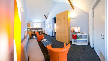 A modern living room with a sofa, orange chairs, a dining table, and a kitchen in the background.