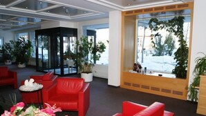 A lobby with red leather sofas, potted plants, and a large window with a view of a snowy landscape. - Hotel Alvier (Wartau)