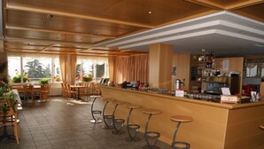 A bar area with a long counter, multiple stools, and a seating area with tables and chairs. - Hotel Alvier (Wartau)