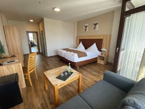 A hotel room with a bed, a wooden desk, a small table with wine glasses, a sofa, and a mirror. - Hotel Roeb (Nideggen)