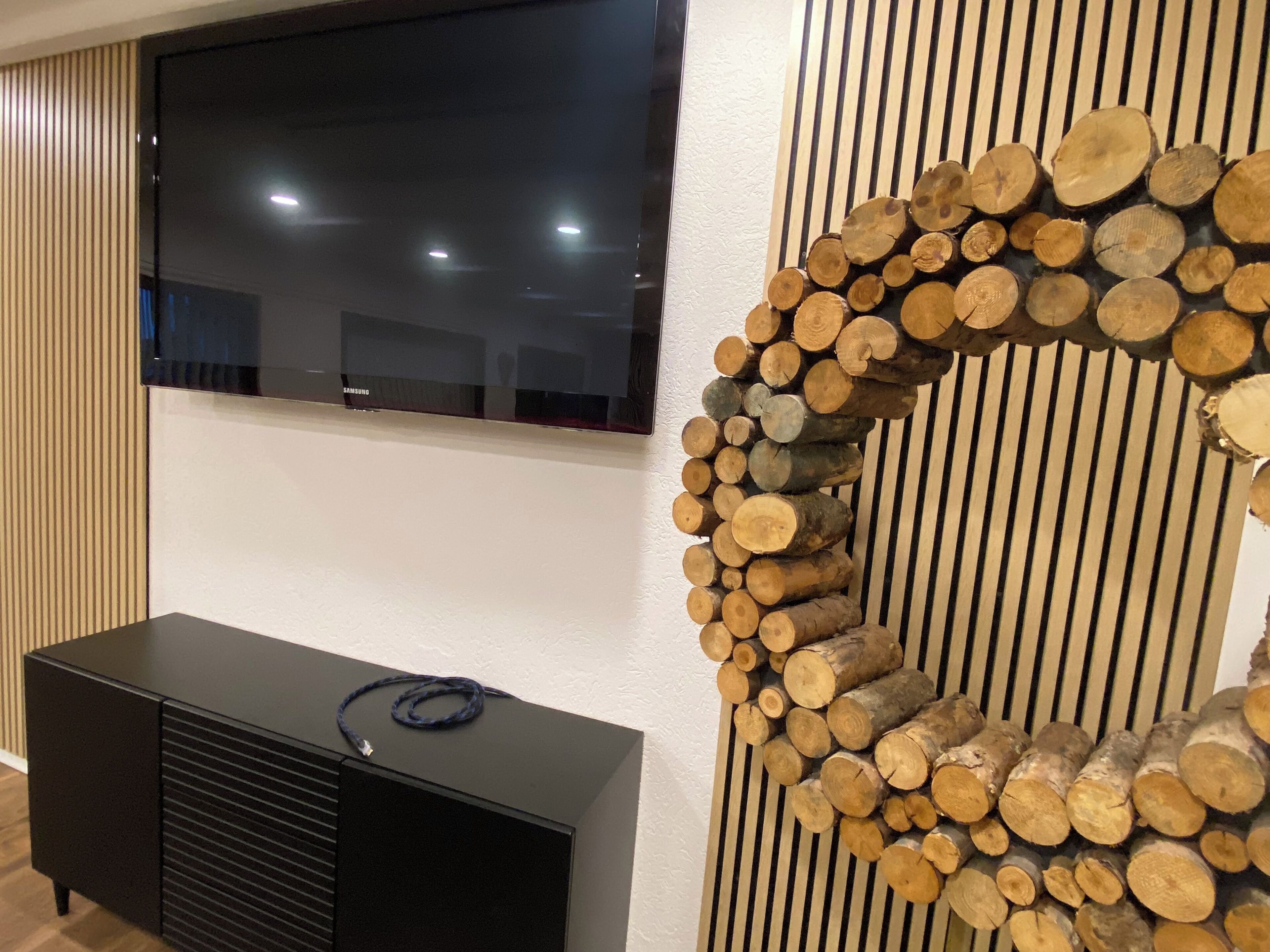 Ein flachbildfernseher an der Wand, darunter eine schwarze Unterhaltungsanlage und eine dekorative Wand aus Holzstämmen.