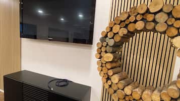 Ein flachbildfernseher an der Wand, darunter eine schwarze Unterhaltungsanlage und eine dekorative Wand aus Holzstämmen.