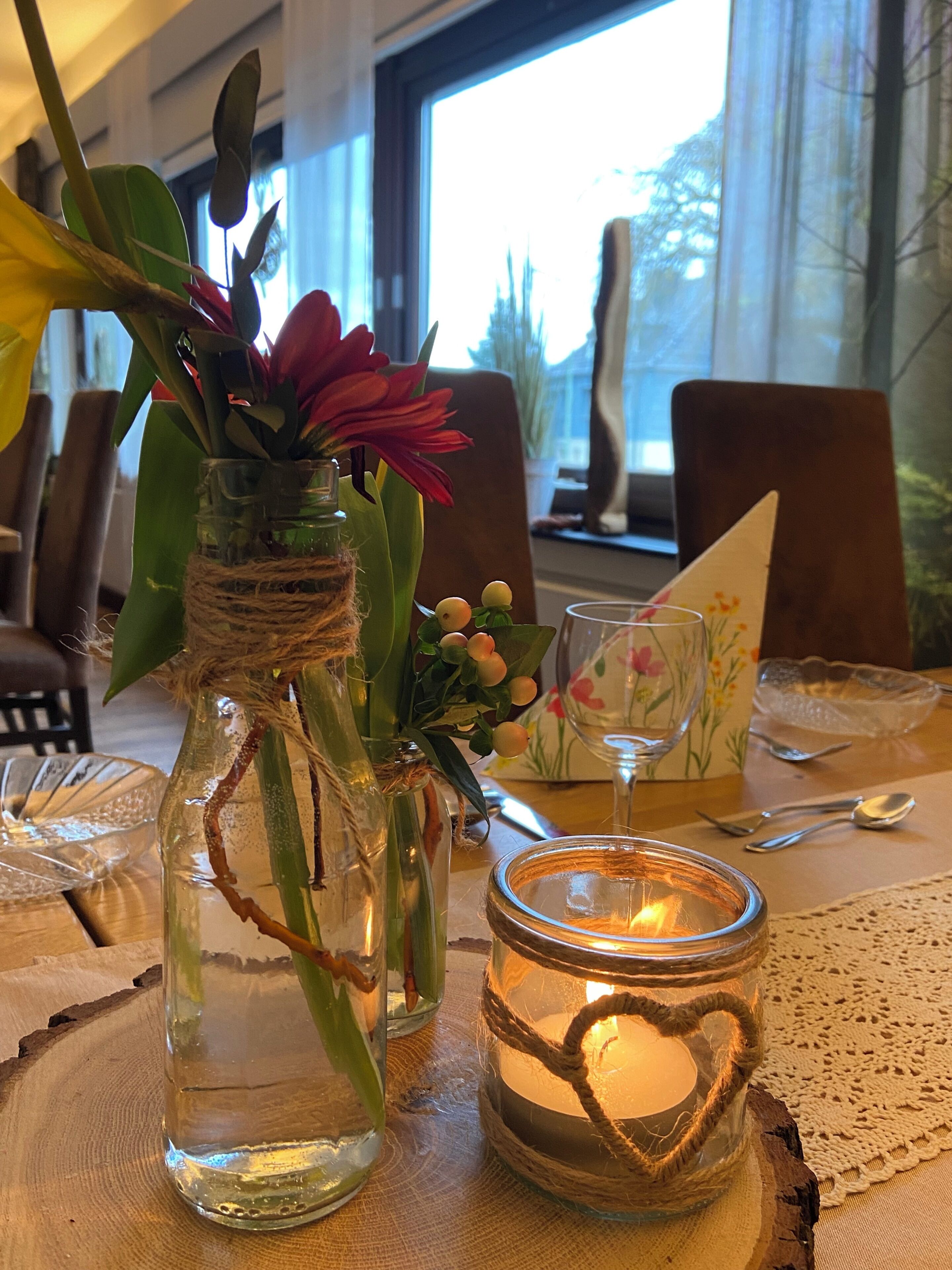 A dining table with a candle, a glass jar with a plant, and a decorative item.