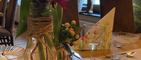 A dining table with a candle, a glass jar with a plant, and a decorative item.