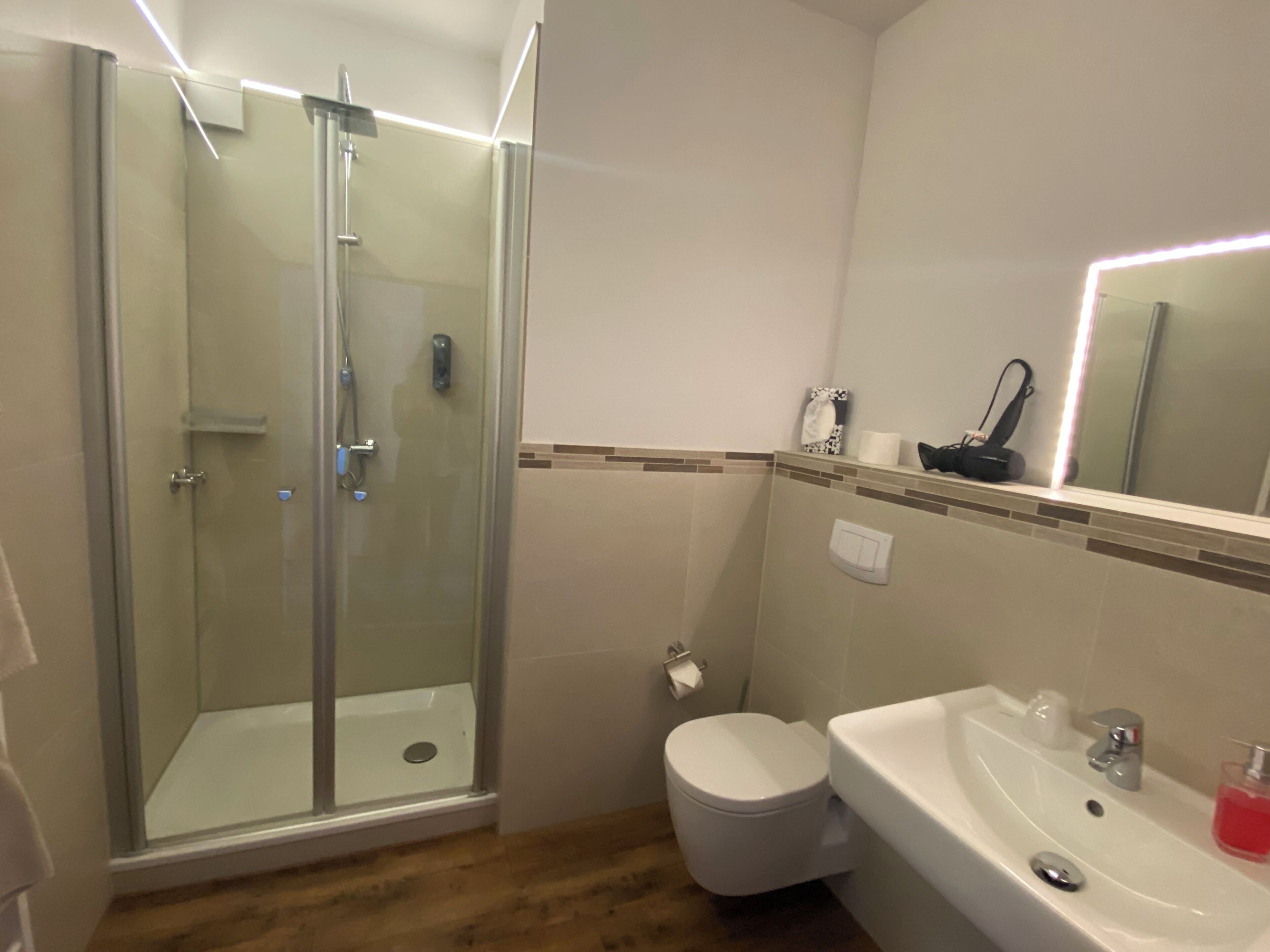 Et badeværelse med en brusekabine i glas, toilet og et spejl over vasken.