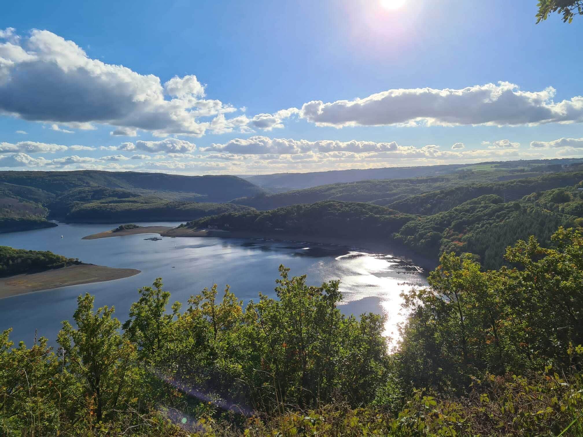 A panoramic view of a lake surrounded by hills and dense forest.