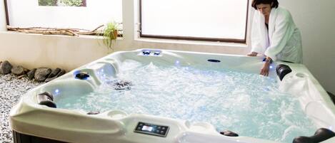 A hot tub with a control panel, surrounded by rocks and a window with a view of greenery.