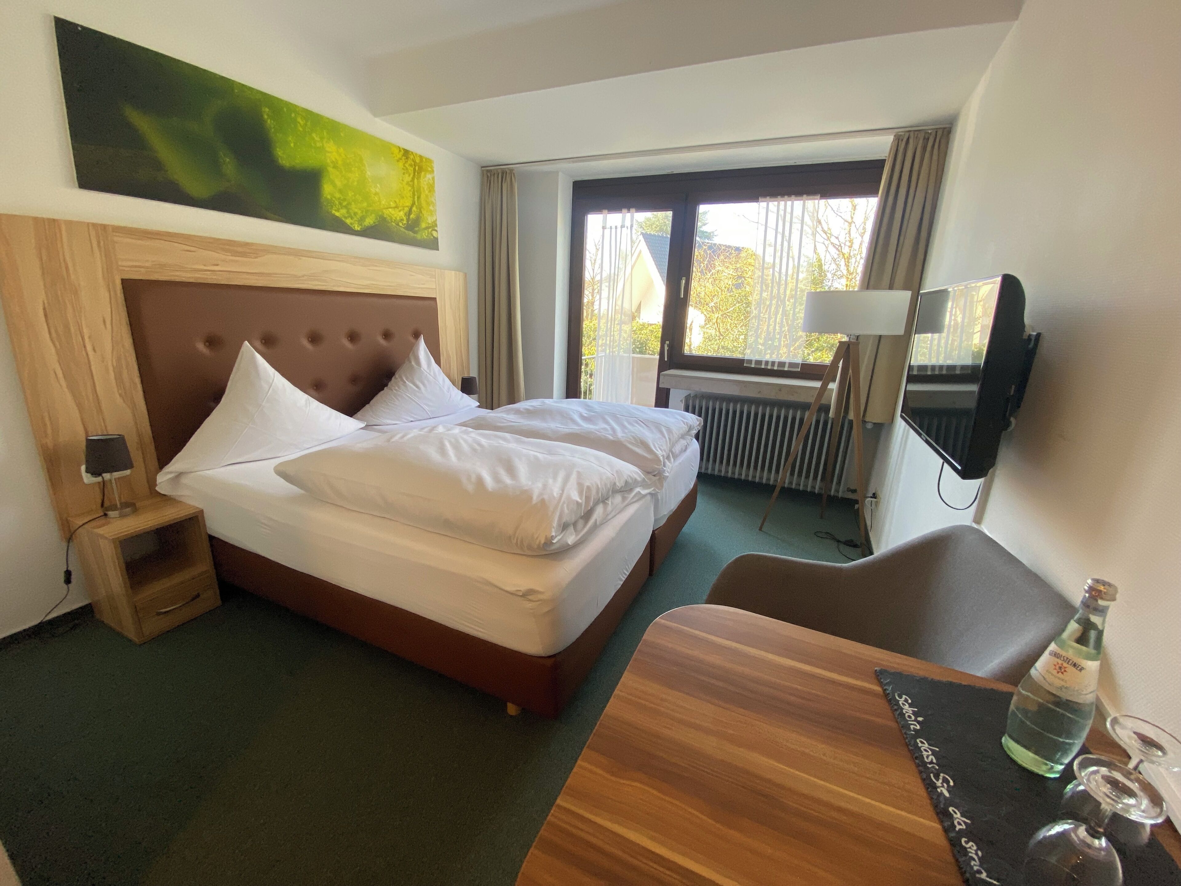Ein Hotelzimmer mit Bett, Fernseher, Tisch mit einer Flasche und einem Bild an der Wand.