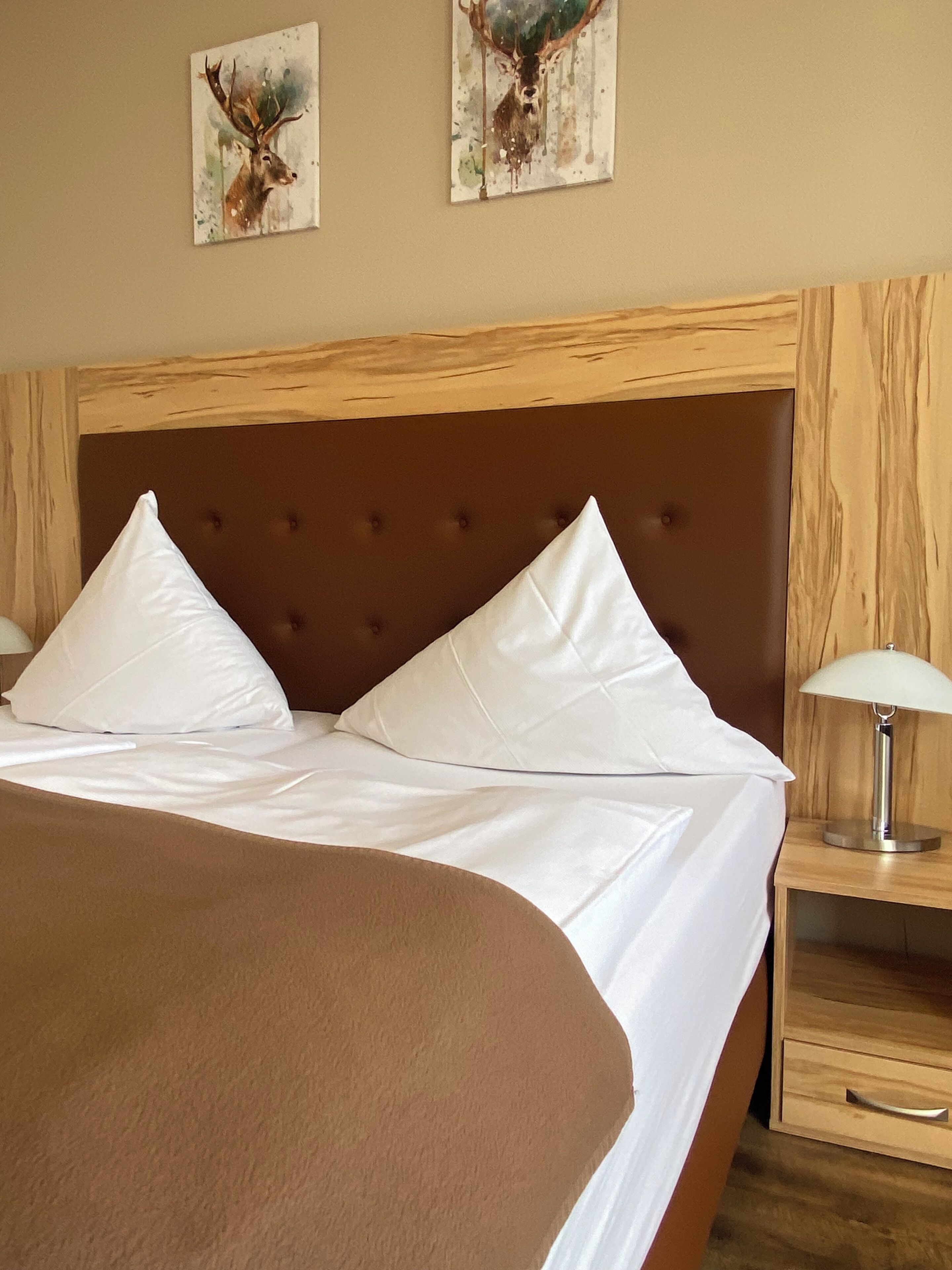 A bed with white linens, two pillows, and a brown headboard in a hotel room.