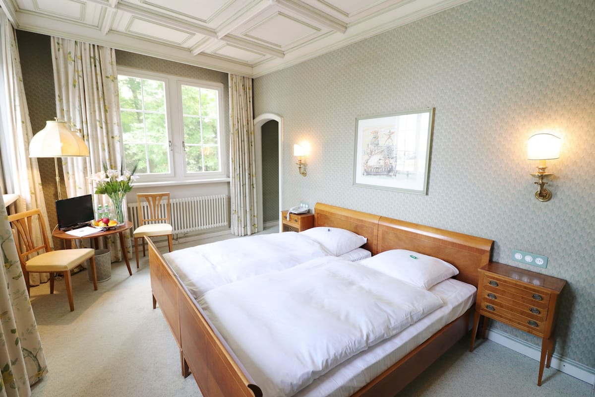 Une chambre d’hôtel avec un grand lit, un bureau avec un ordinateur, une chaise et une fenêtre avec des rideaux.