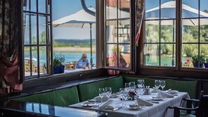 Un comedor con mesas dispuestas para una comida, ventanas amplias con vistas al mar y sombrillas exteriores.