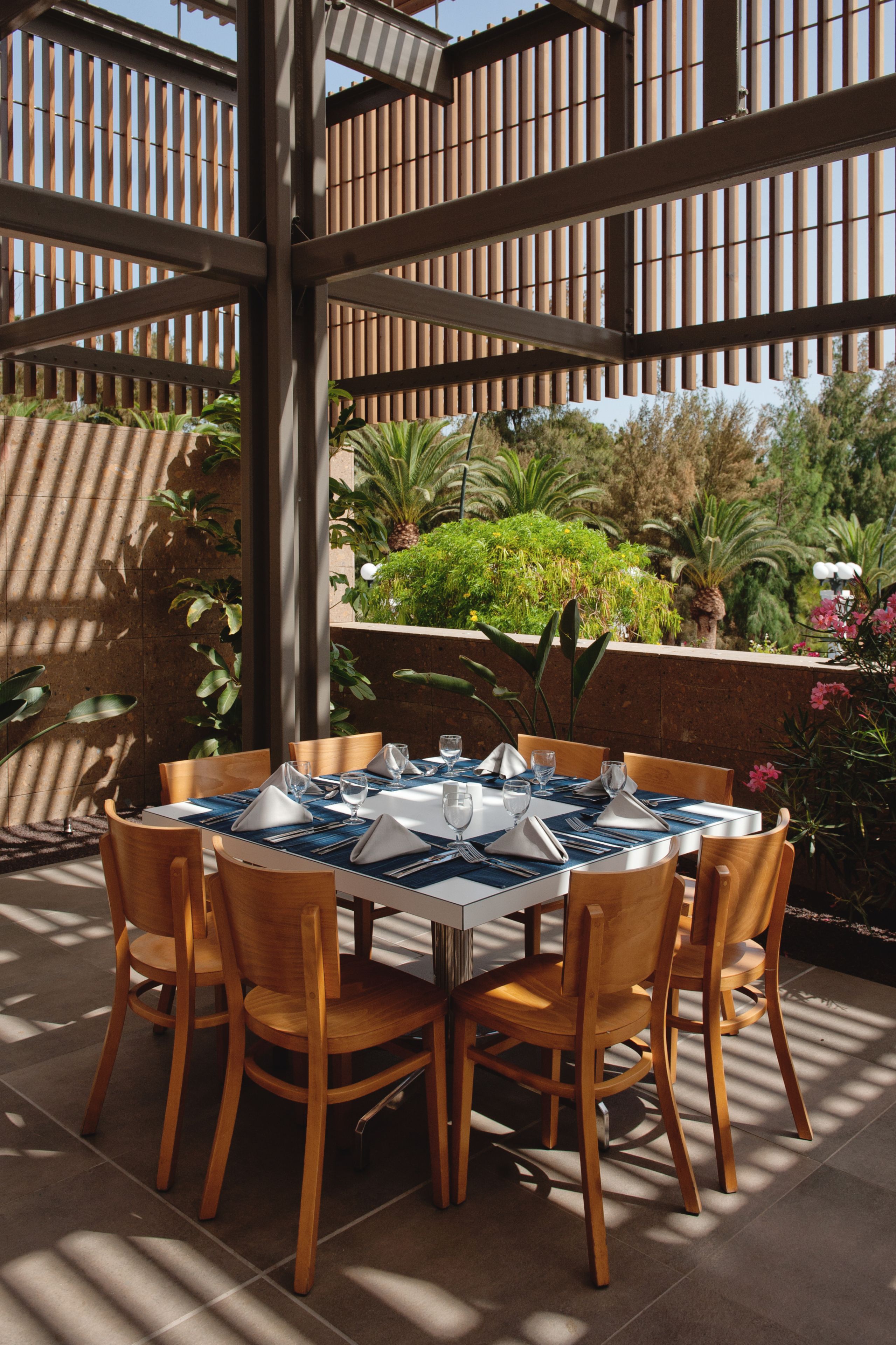 Un área de comedor al aire libre con una mesa redonda preparada para seis personas, rodeada de sillas de madera.