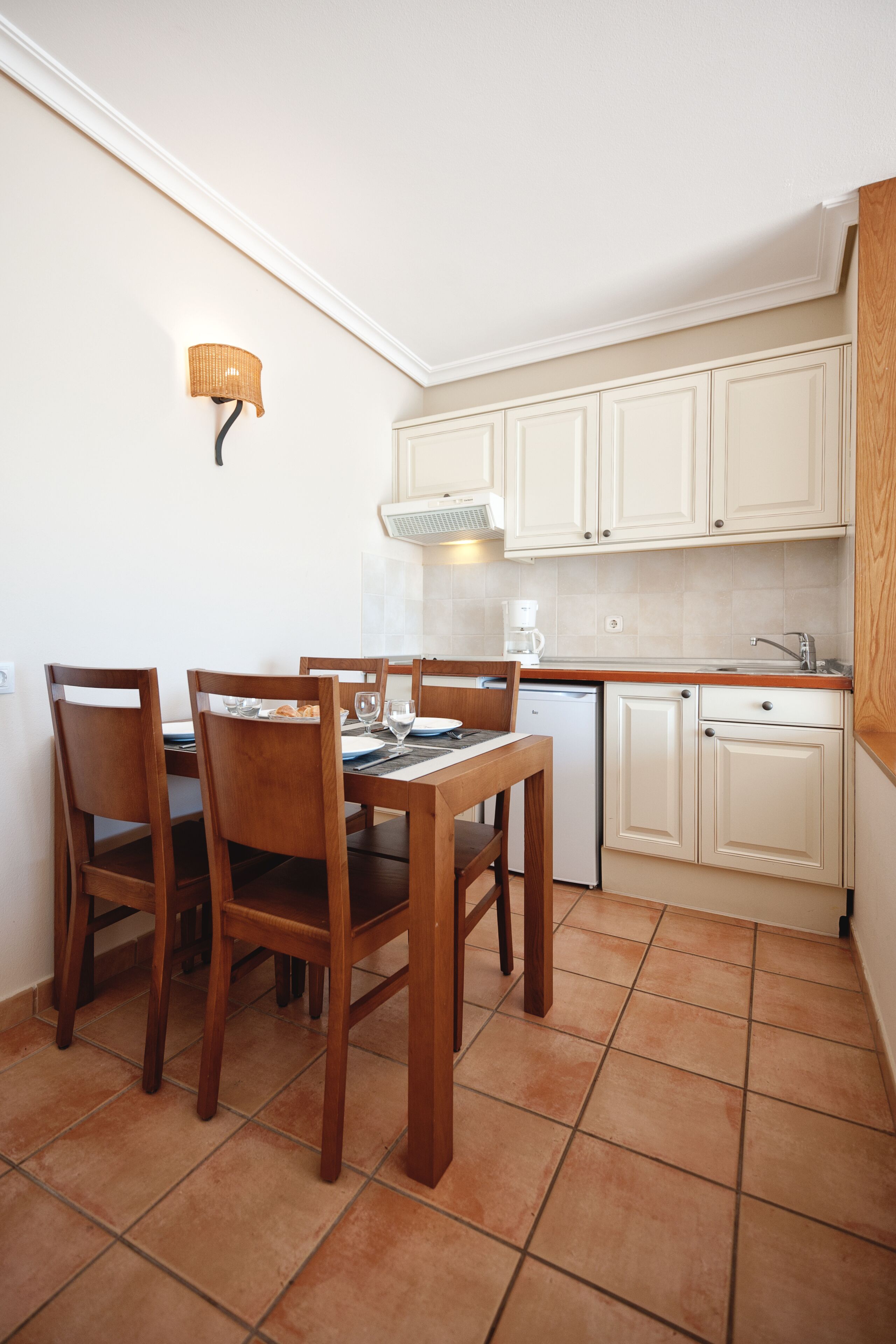 A compact kitchen with white cabinets, a dining table with chairs, a coffee maker, and a dishwasher.