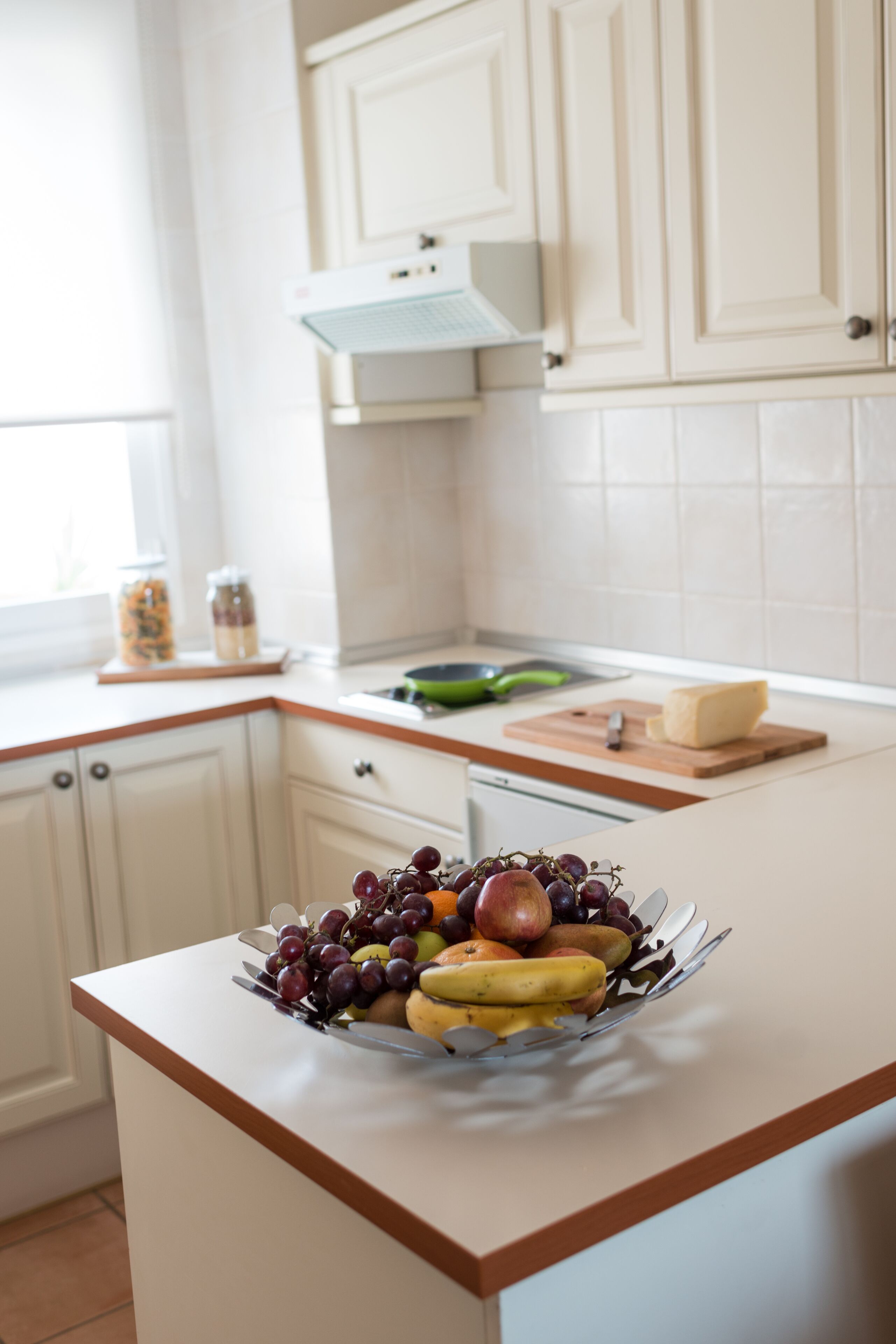Una cocina con armarios blancos, un frutero en la encimera y una ventana con luz natural.