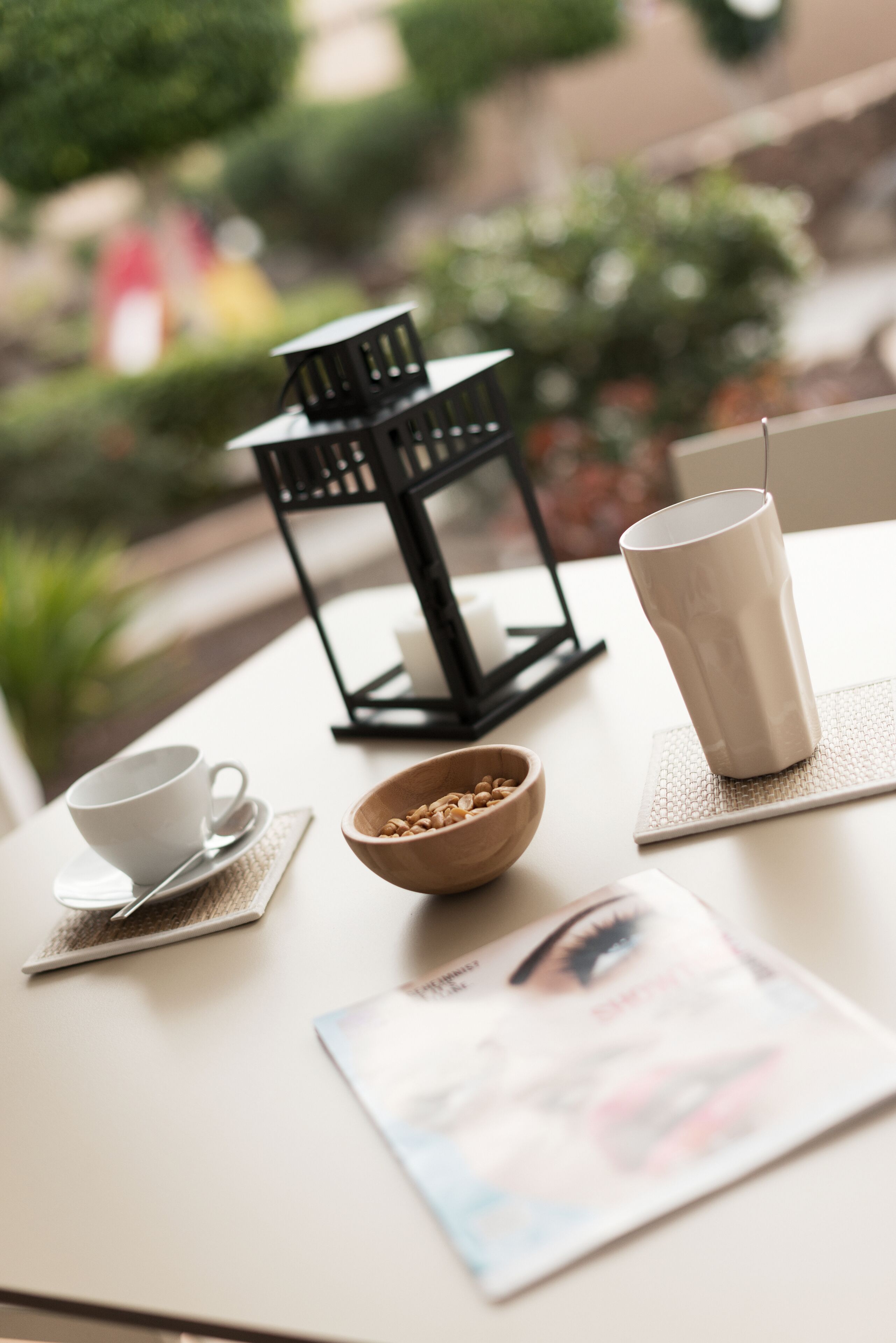 Una mesa con una taza blanca, un platillo, un bol de madera, una taza de cerámica blanca y una revista.