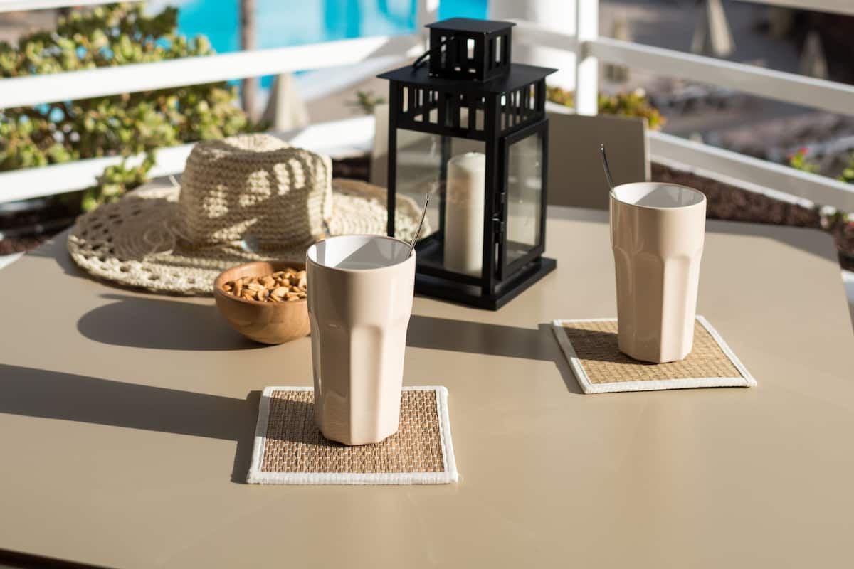 Una mesa con dos tazas, un farol y un bol de nueces, con vista a una piscina y palmeras.