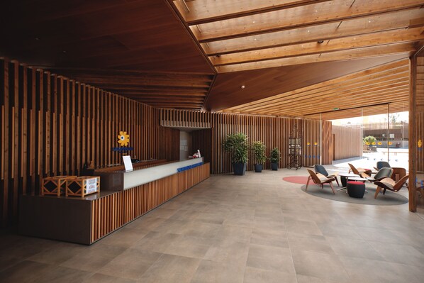 A spacious lobby with a wooden reception desk, seating area, and potted plants. - Sotavento Beach Club (Pajara)