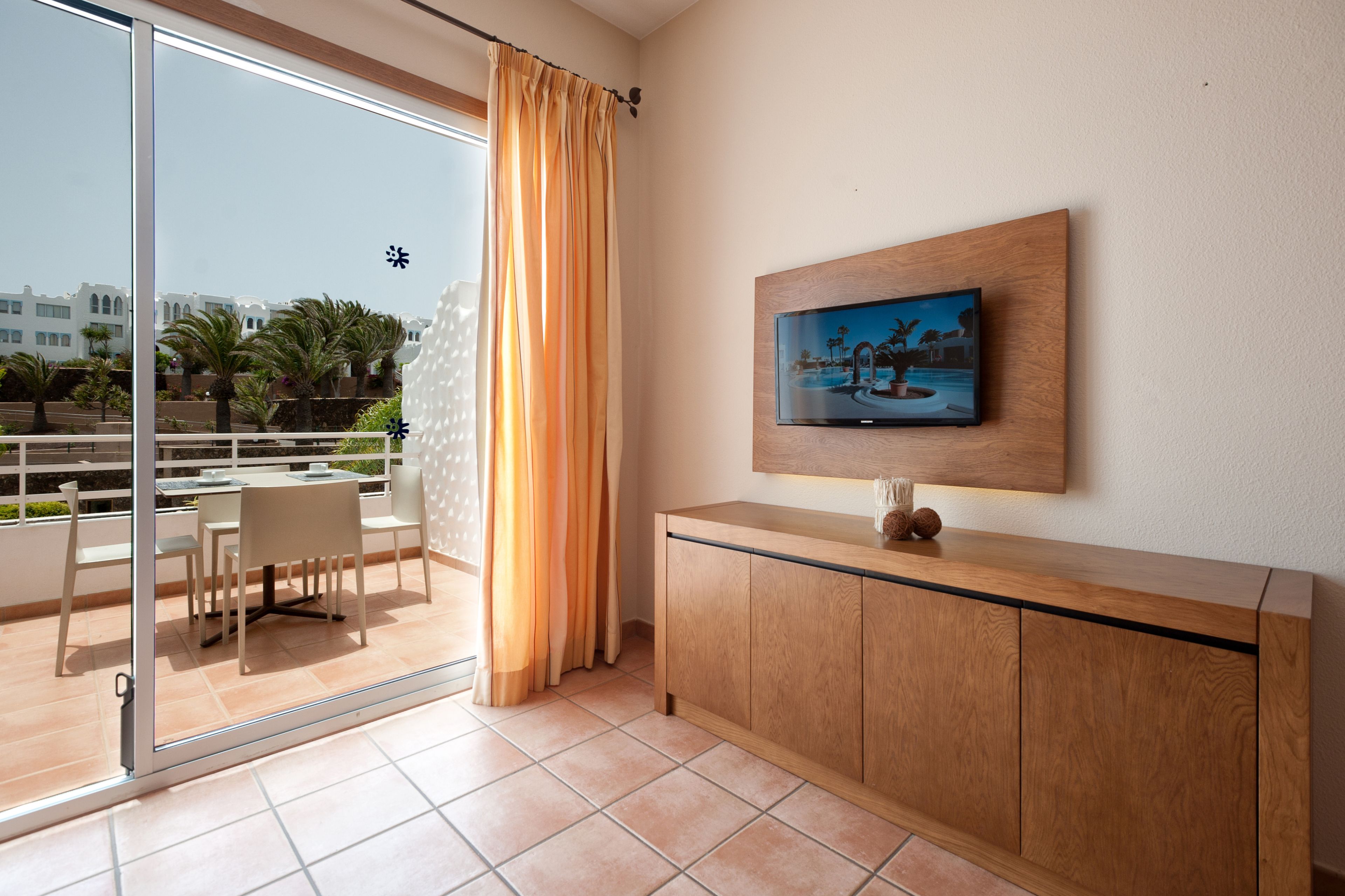 Una camera moderna con una porta in vetro che dà su un balcone, un armadio in legno e un televisore a schermo piatto montato a parete.