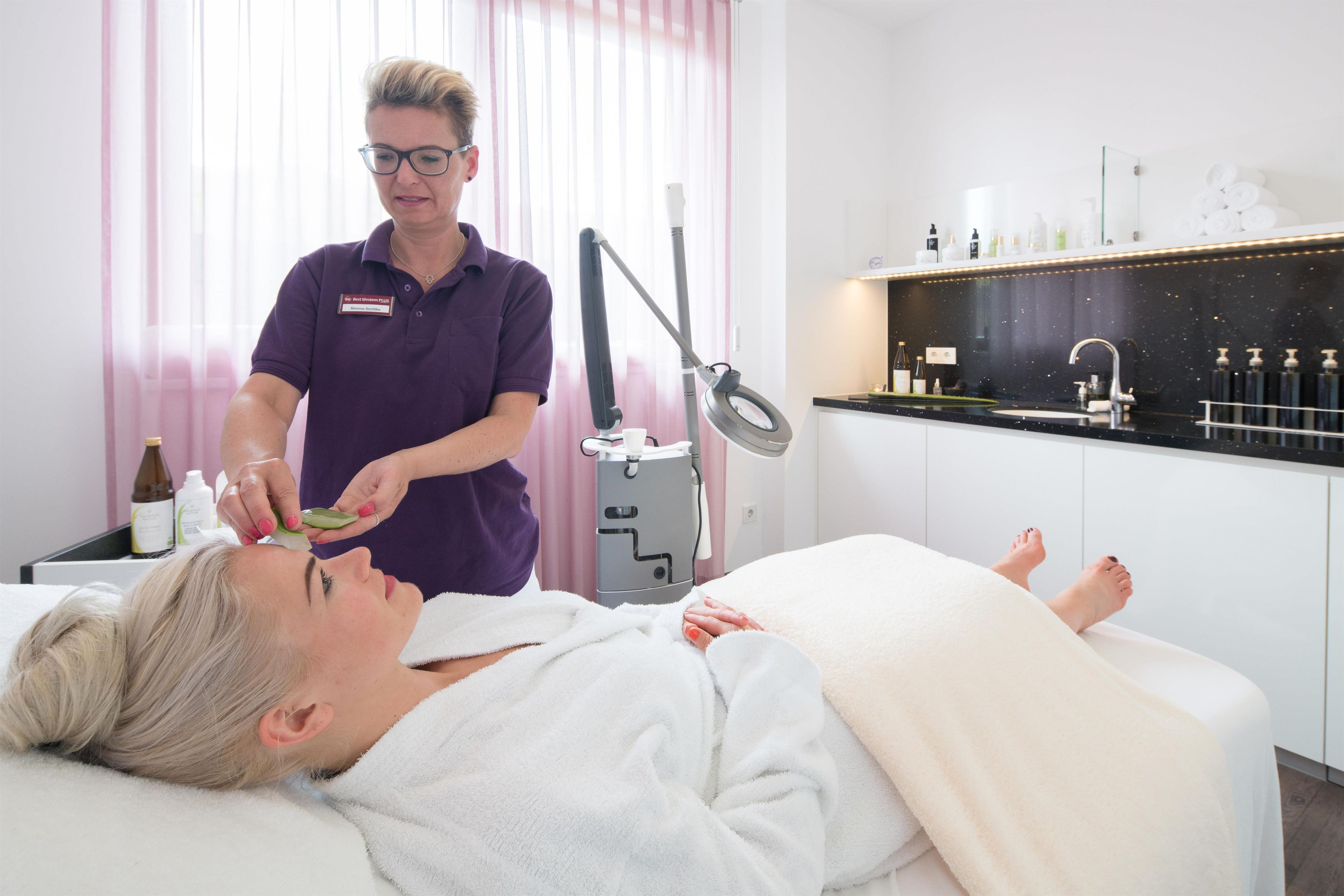 A person lying on a treatment bed receiving a facial treatment from a professional in a clinical setting with a modern, clean design.