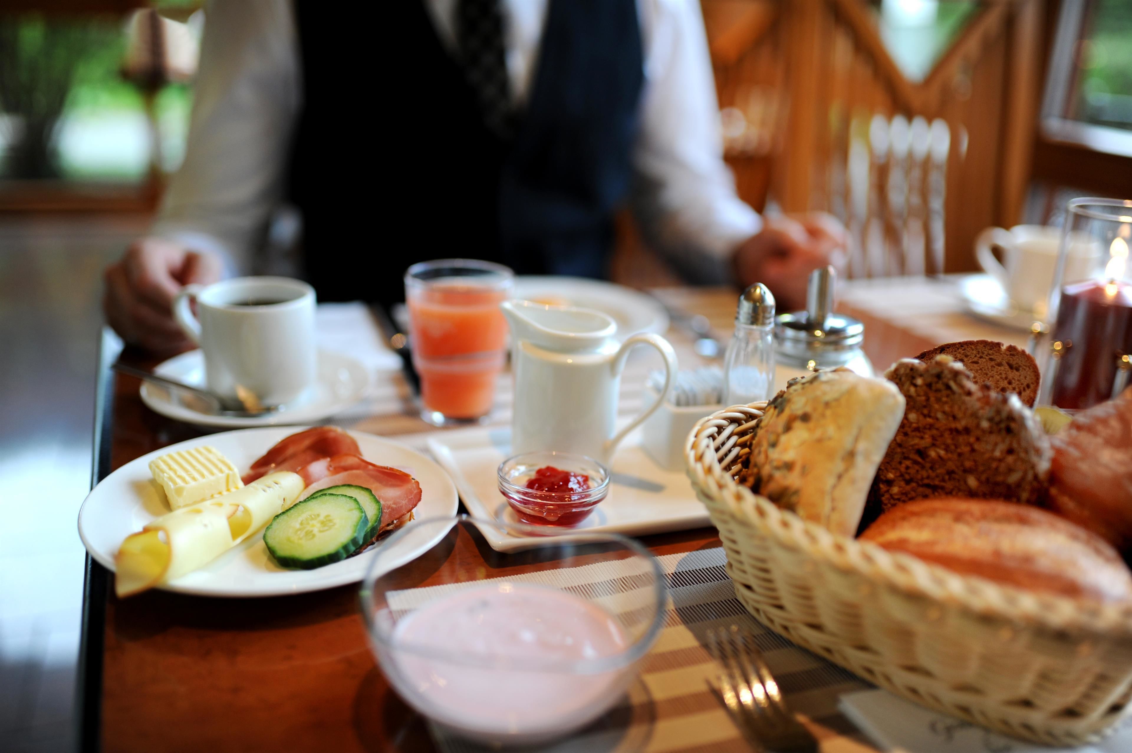 Een ontbijtsetting met borden vol eten, een koffiekop, een glas sap en een kaars op een tafel.