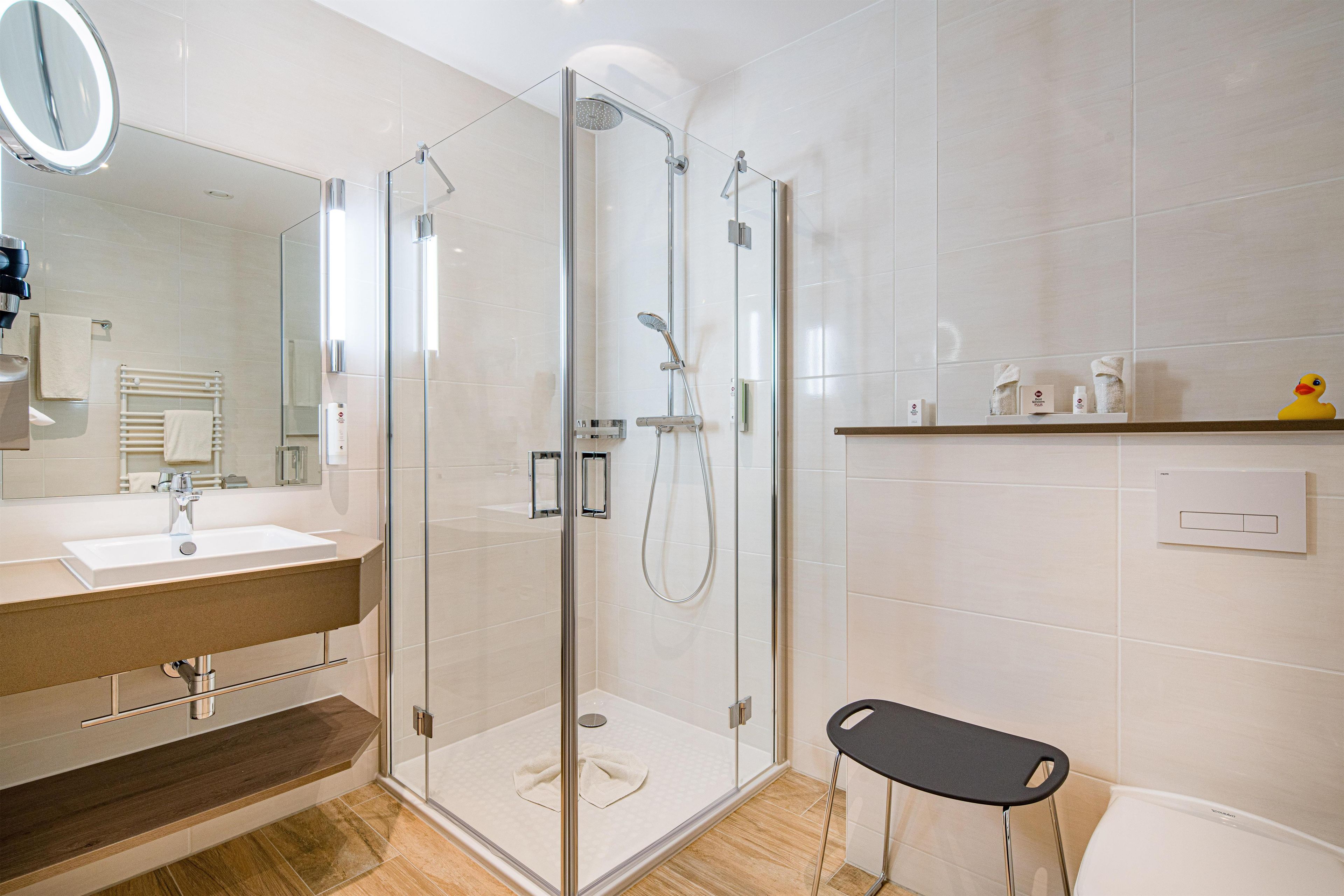 Ein modernes Badezimmer mit einer Glaskabine zur Dusche, einem Waschtisch mit Spiegel und einer Toilette.