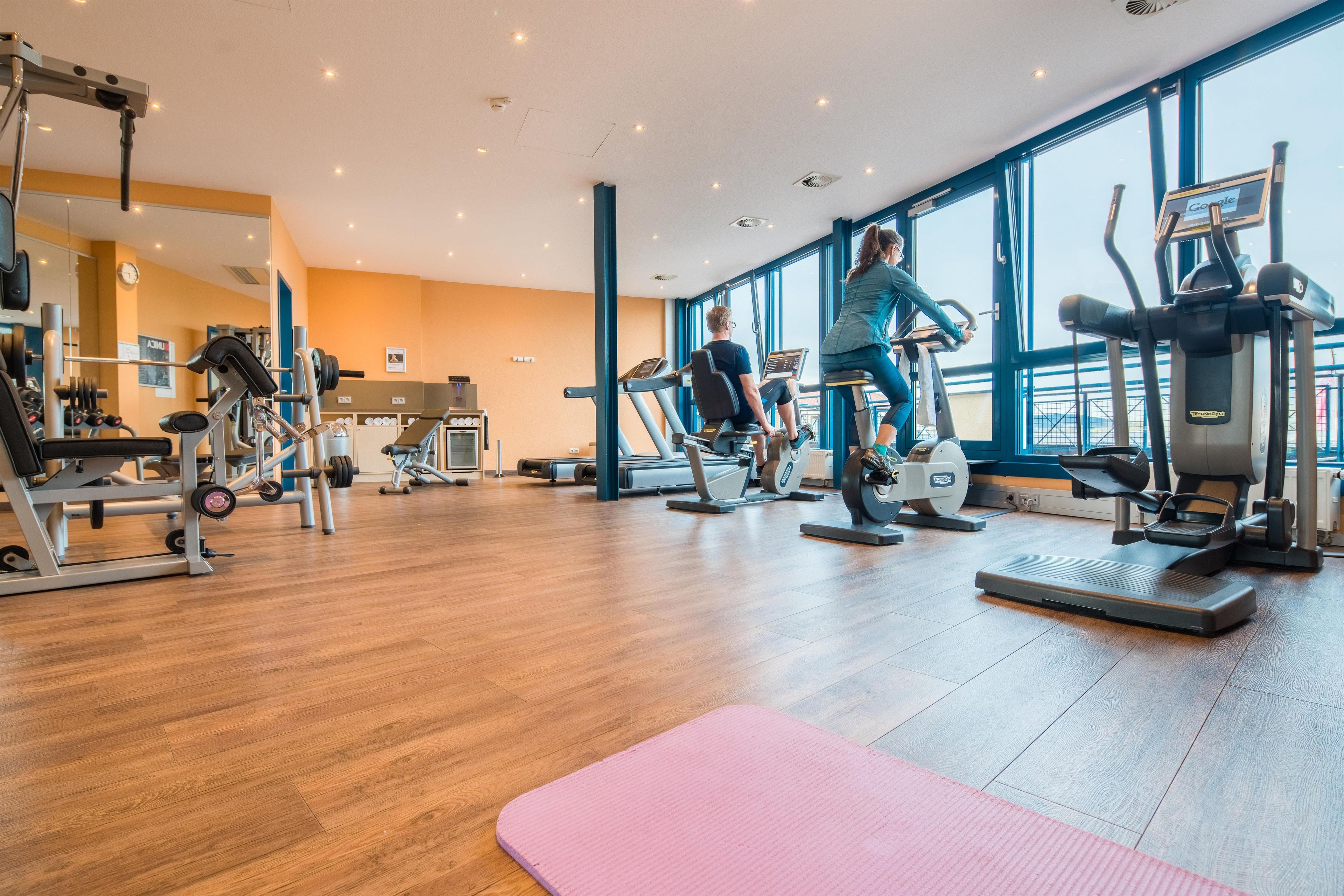 A gym with cardio machines, weightlifting equipment, and a wooden floor.