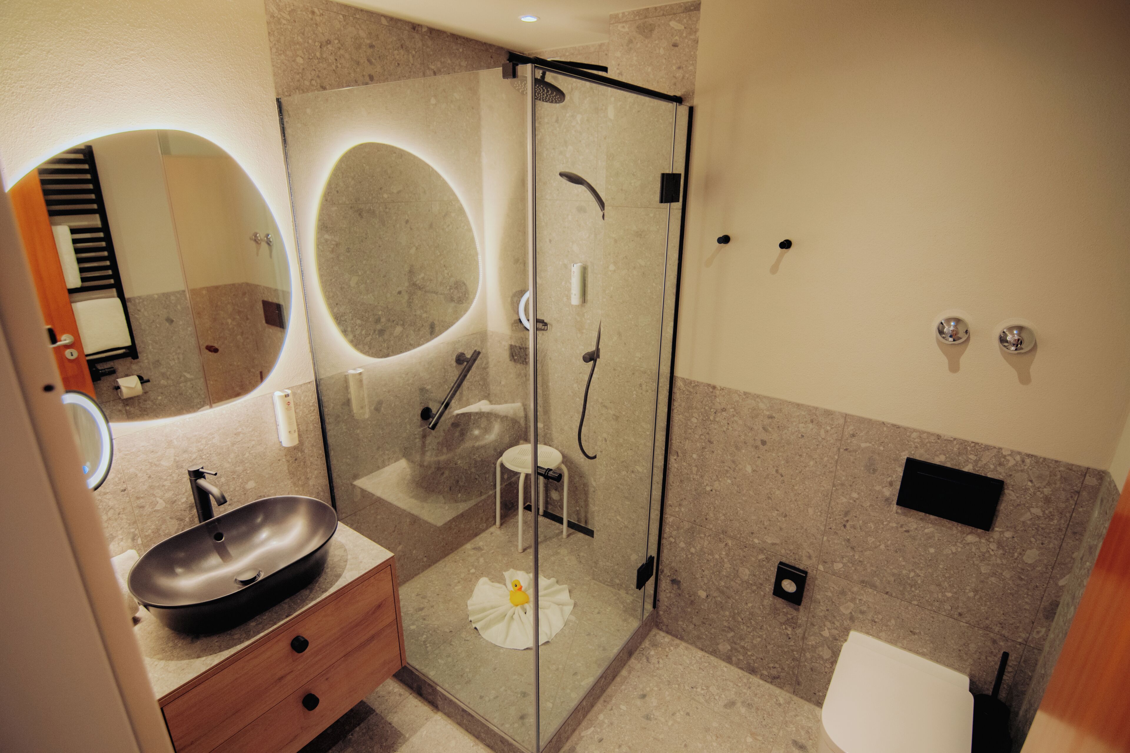 A modern bathroom with a round mirror, a sink, a glass-enclosed shower, and a toilet.