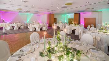 Ein Festsaal mit runden Tischen, gedeckt für ein Essen, jeweils mit weißen Tischdecken und Kerzenarrangements in der Mitte.