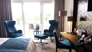 Een hotelkamer met een bed, twee fauteuils, een kleine tafel, een bureau, een lamp en uitzicht op de omgeving.
