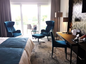 Een hotelkamer met een bed, twee fauteuils, een kleine tafel, een bureau, een lamp en uitzicht op de omgeving.