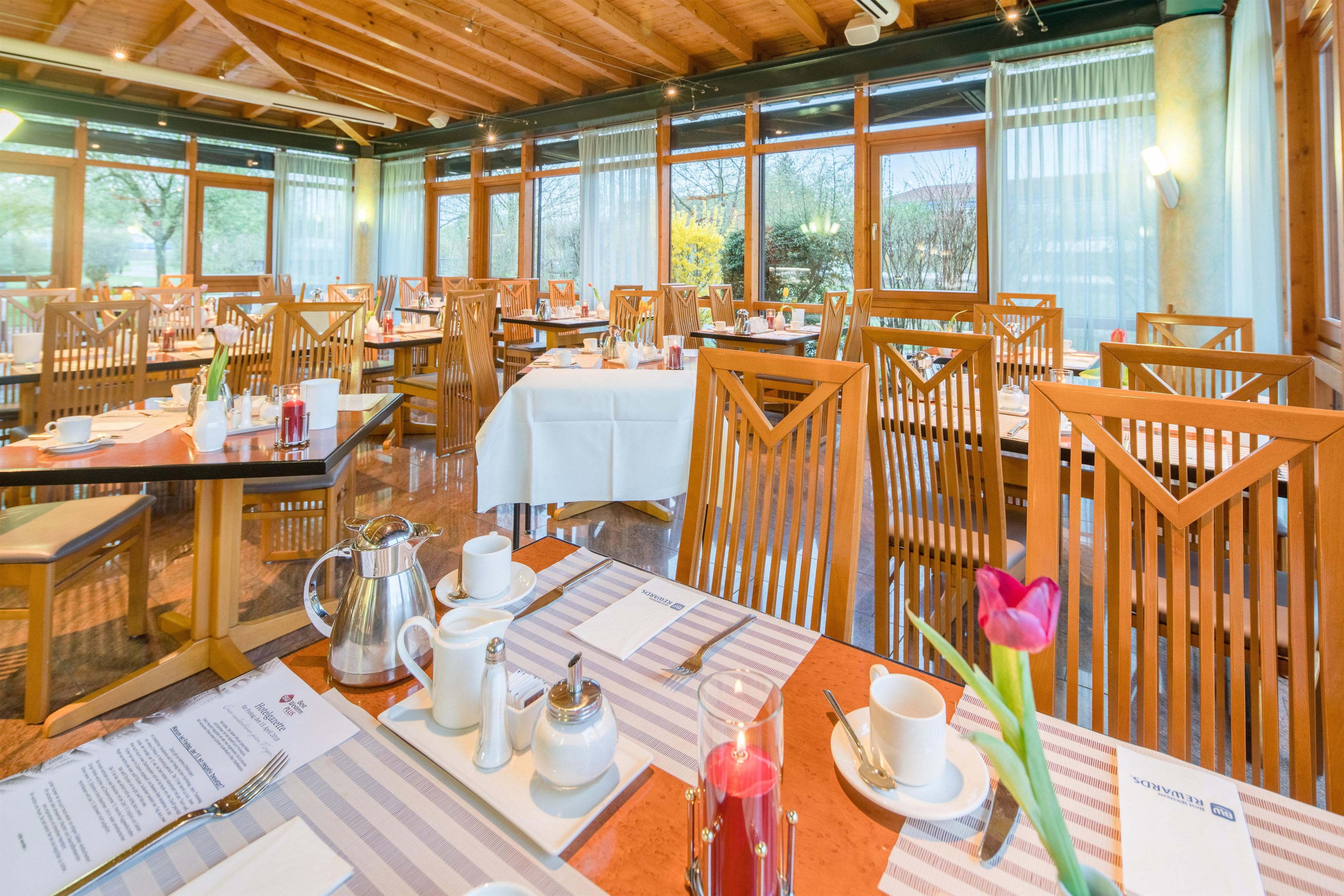 A restaurant with wooden chairs and tables, large windows, and a menu on the table.