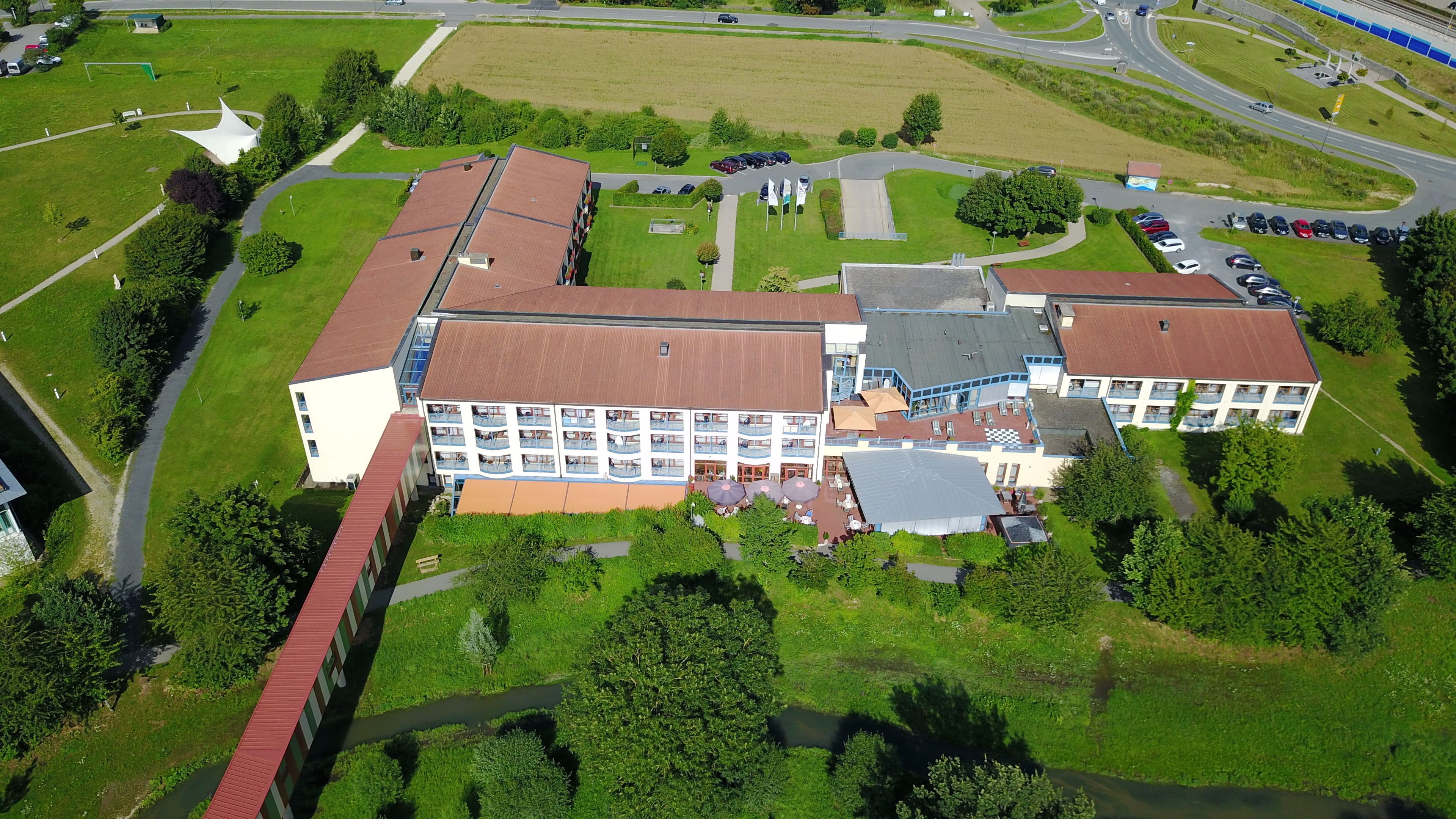 Luftaufnahme eines Hotels mit mehreren Gebäuden, einem Parkplatz und umgebender Bepflanzung.