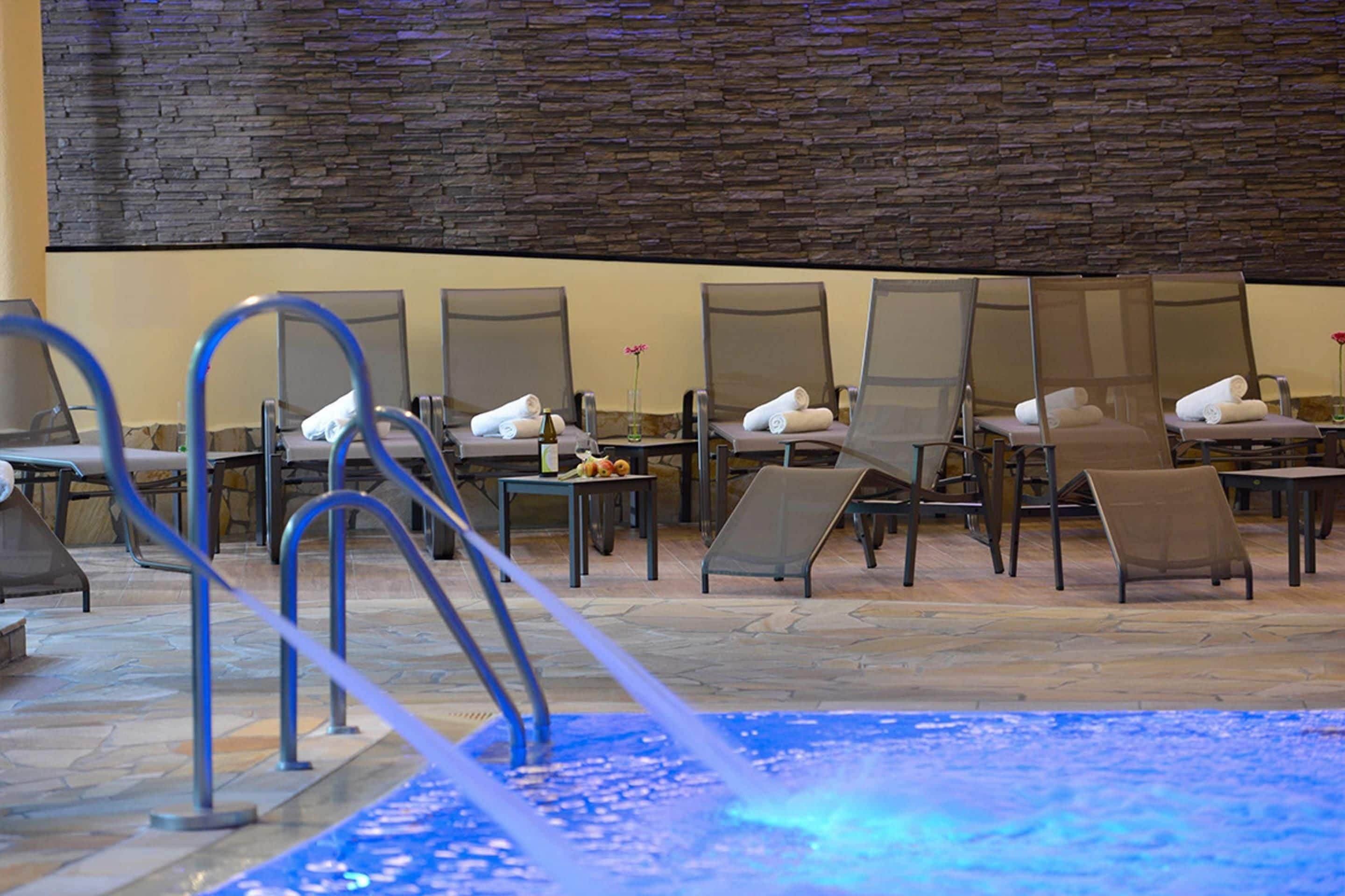 A pool area with lounge chairs and a stone wall.