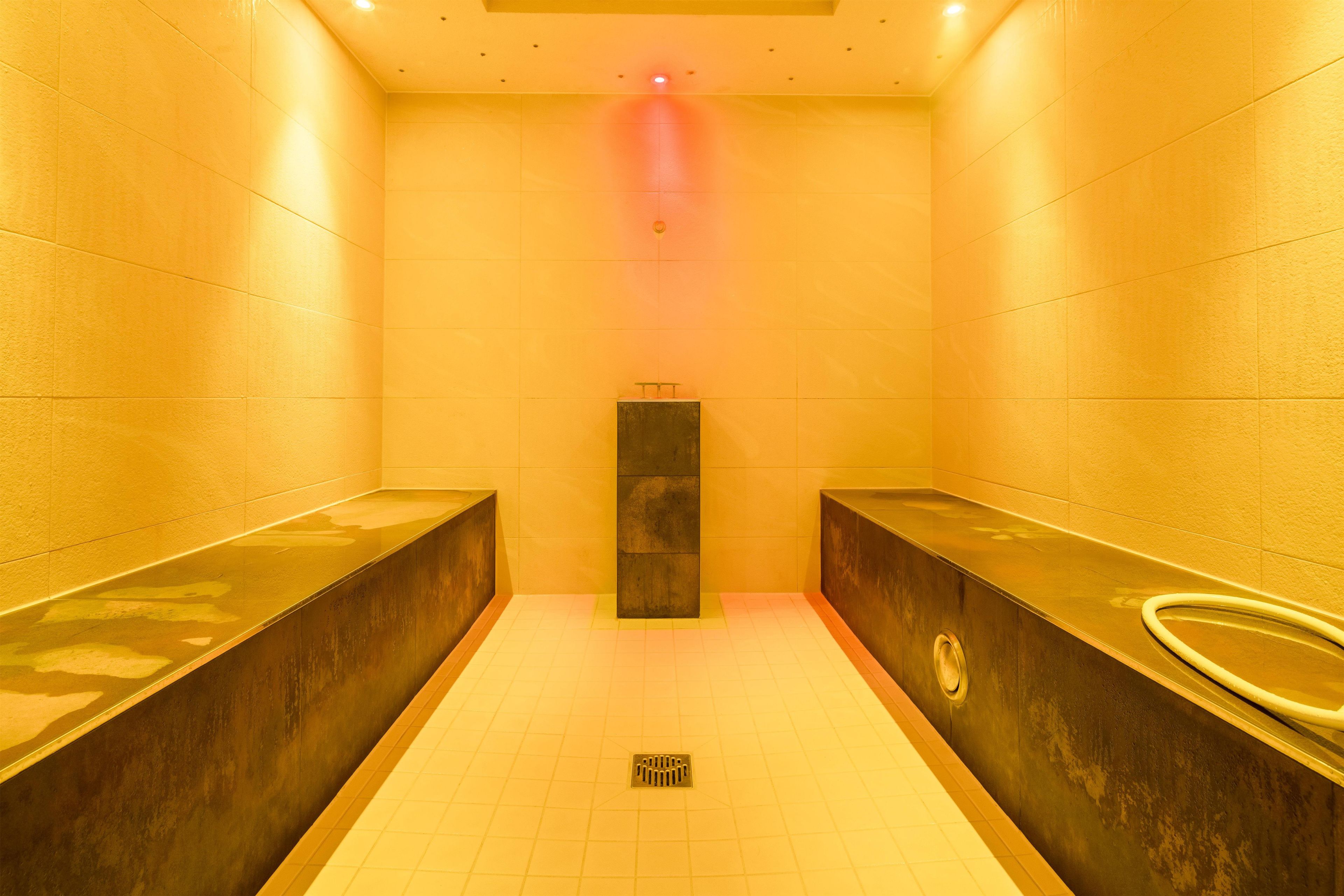 Um sanitário com duas pias, um ralo central e uma luz vermelha no teto.