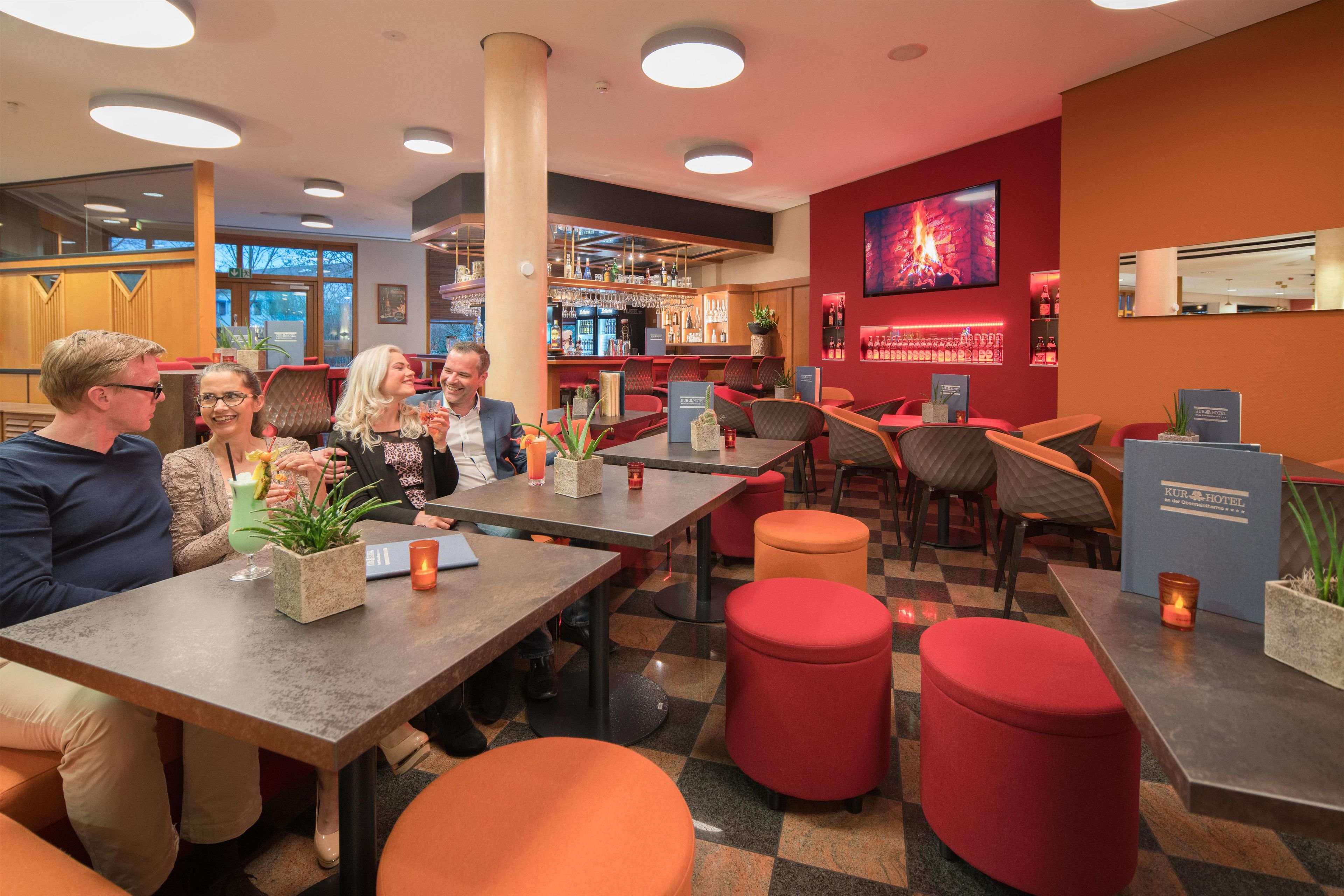A modern bar area with seating, a television screen, and a bar stocked with bottles.