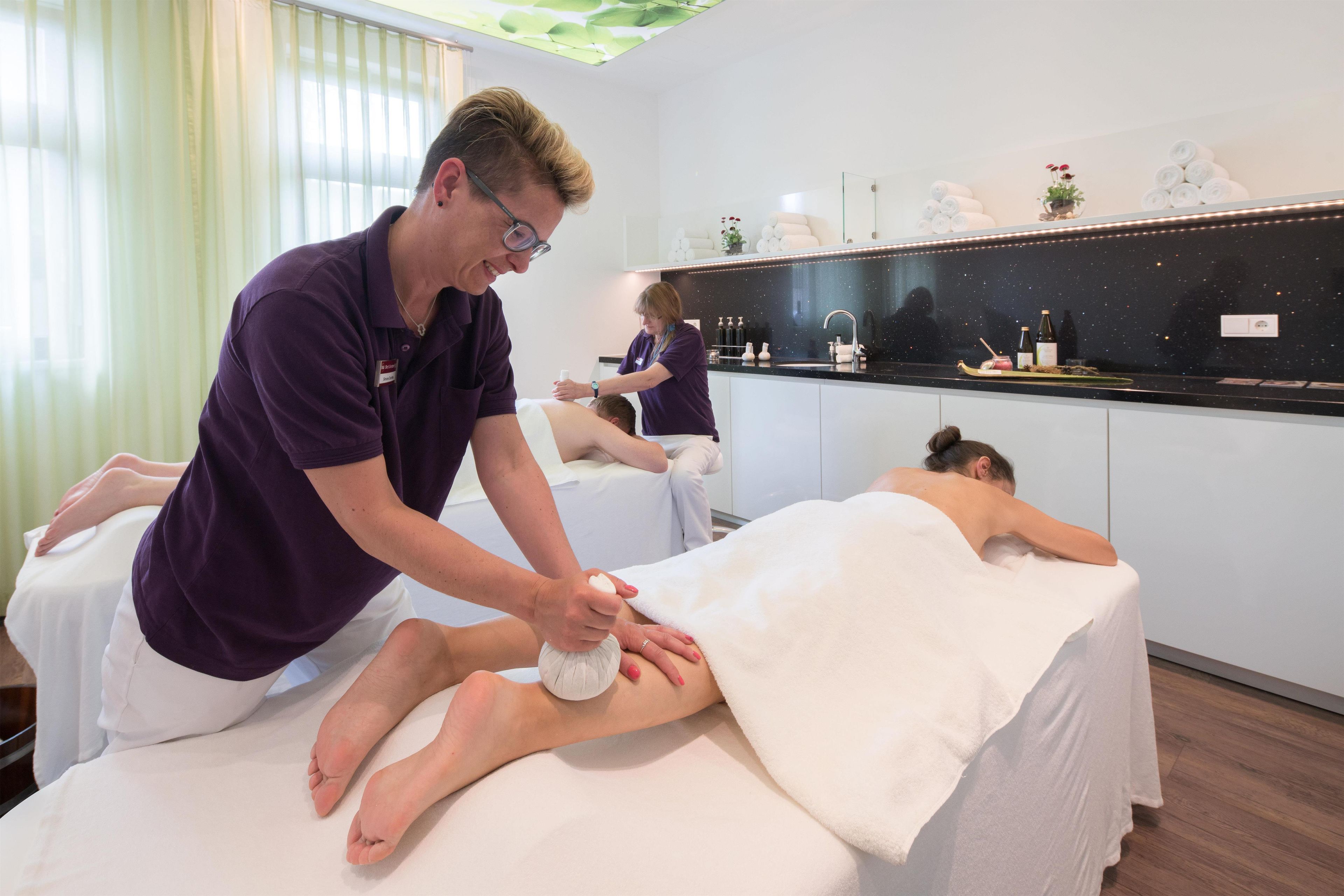 A massage therapy room with a massage table, a client receiving a foot massage, and a therapist attending to another client.