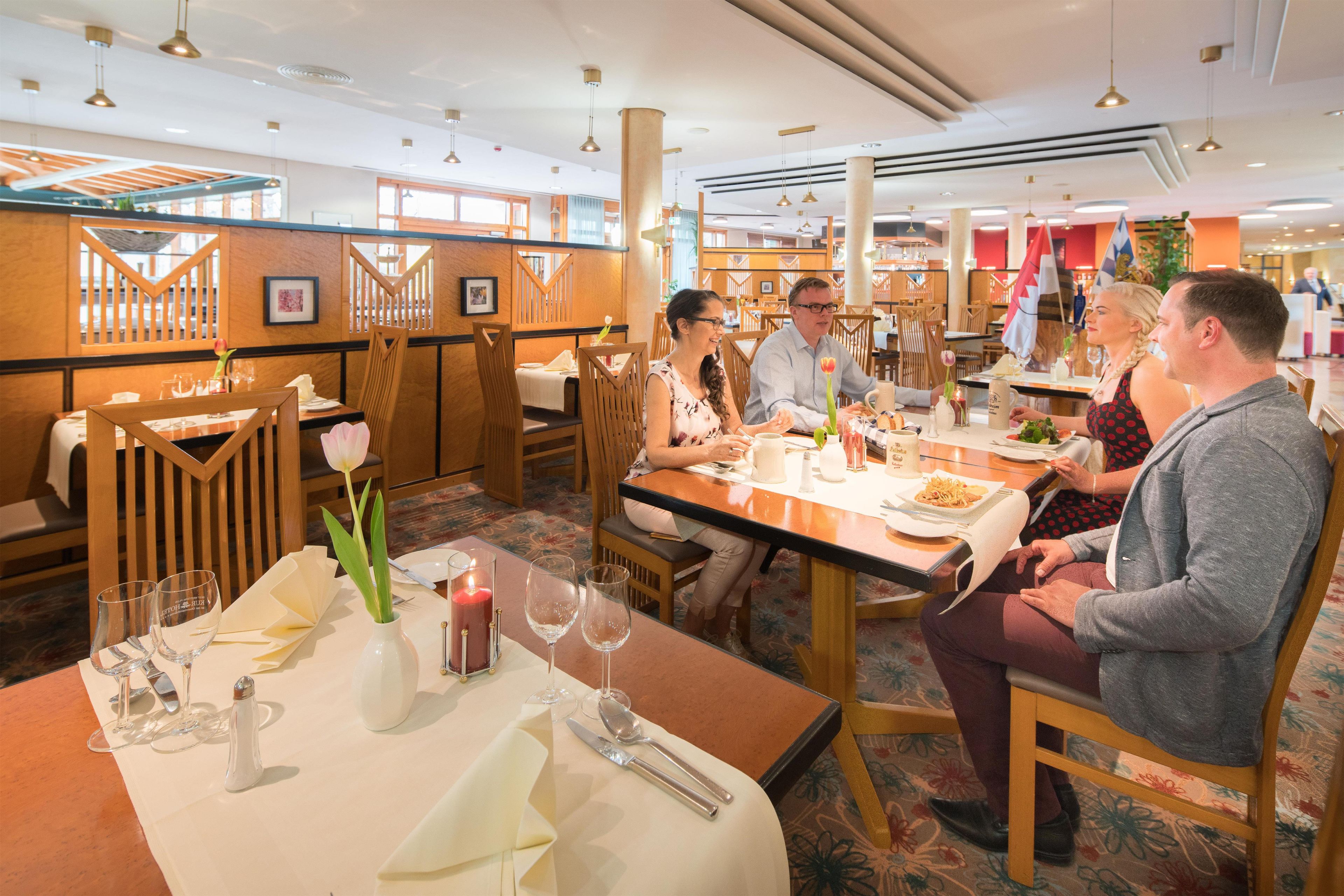 A restaurant with wooden furniture, tables set with plates, glasses, and a candle.