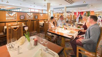 A restaurant with wooden furniture, tables set with plates, glasses, and a candle.