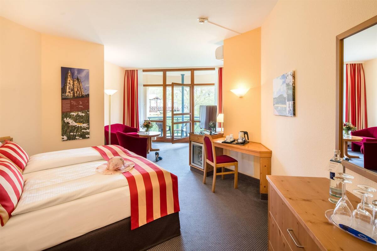 A hotel room with two beds, a desk, a chair, a dresser, and a large window with curtains.