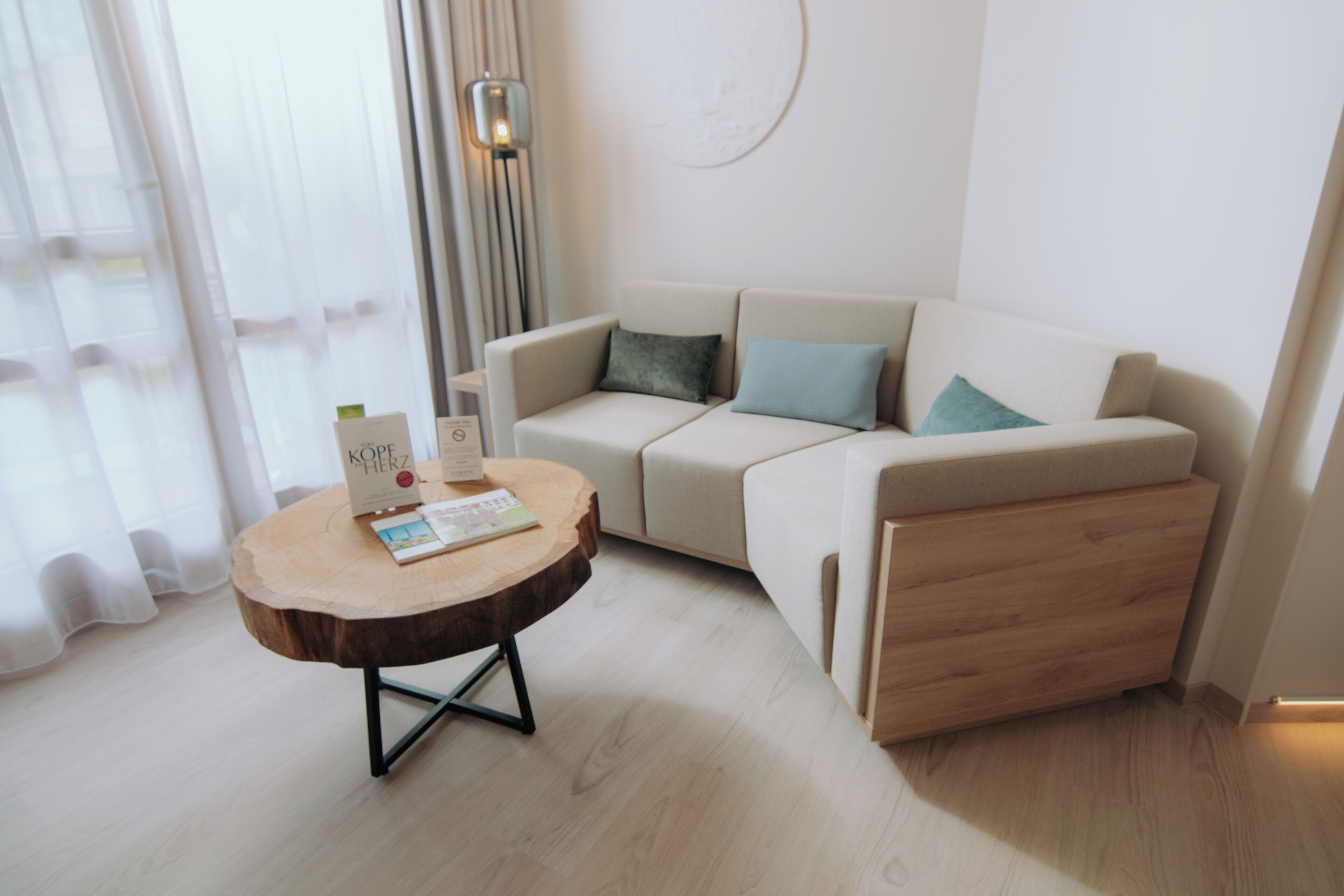 Una sala moderna con una mesa de centro redonda de madera, un sofá beige con cojines y un suelo de tonos claros.