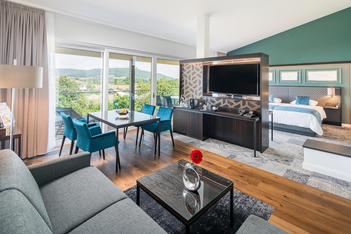 A modern hotel room with a dining area, a TV, and a bed with a view of the outdoors.