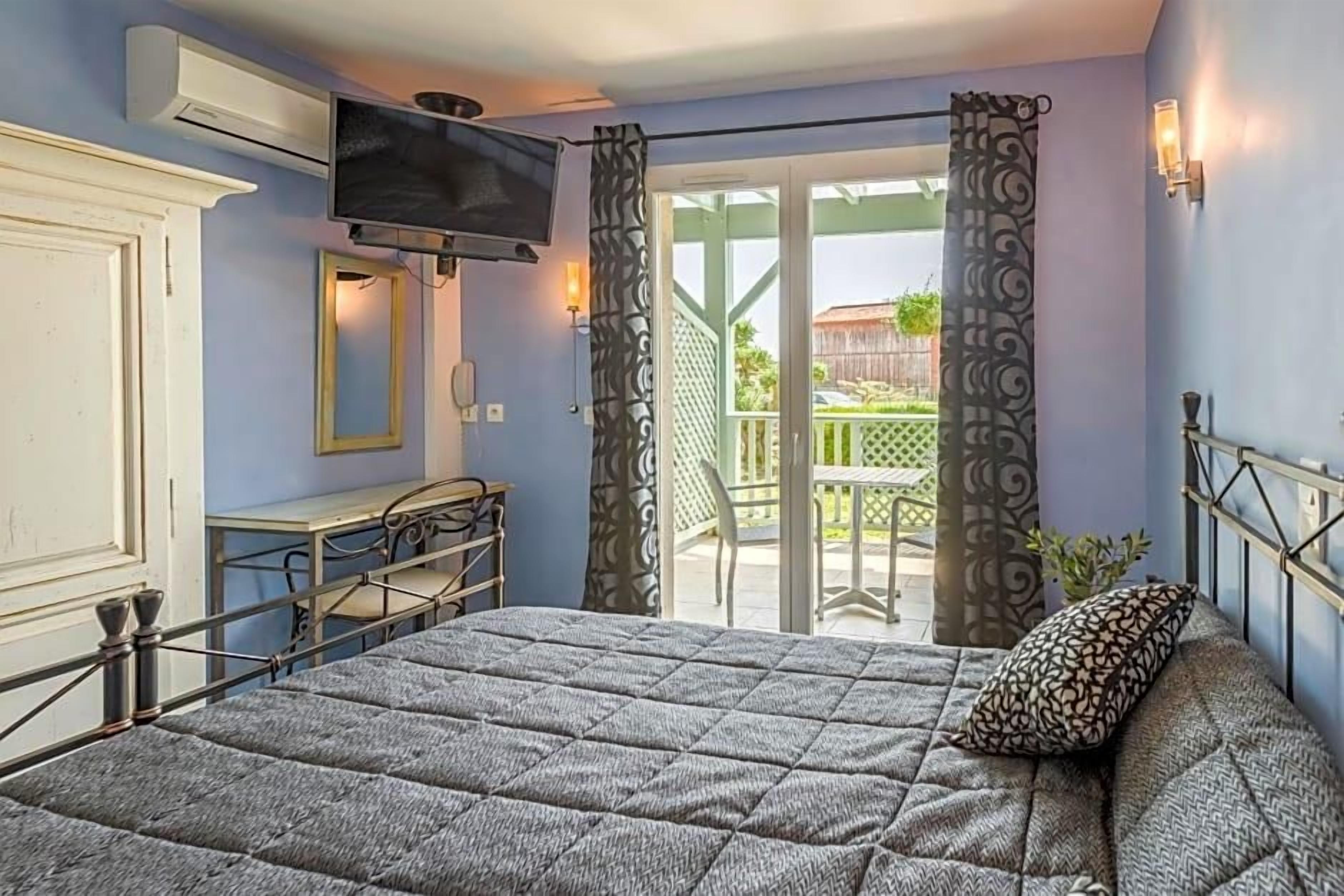 A bedroom with a bed, a television, a desk, and a balcony with curtains.