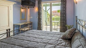 A bedroom with a bed, a television, a desk, and a balcony with curtains.