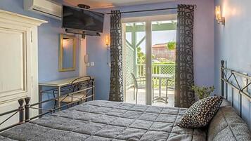 A bedroom with a bed, a television, a desk, and a balcony with curtains.