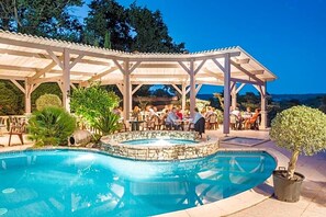 A pool area with a covered seating area and a hot tub.